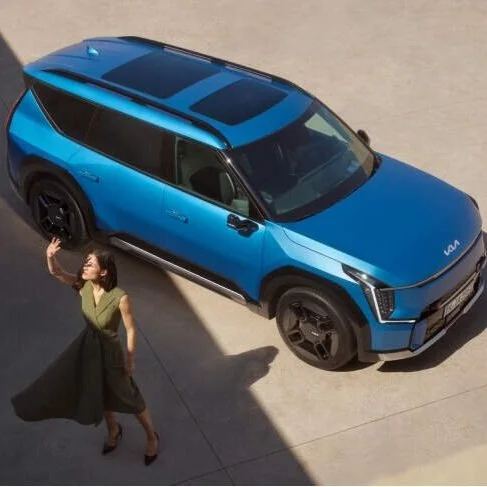 Una donna cammina accanto a un'auto blu elettrica con design moderno, su una superficie di cemento