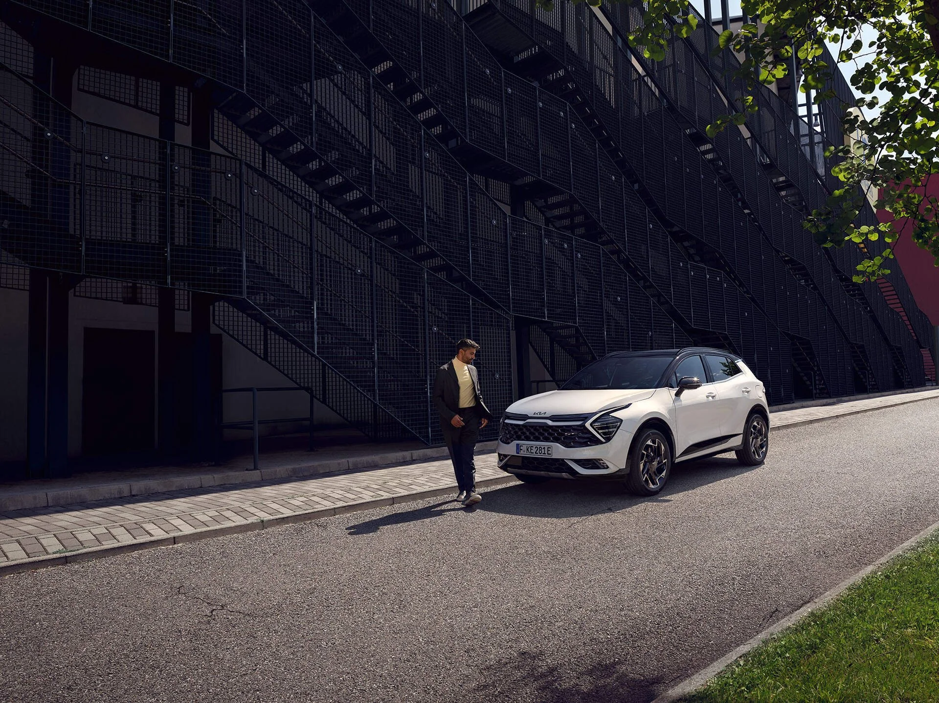 Uomo che si avvicina a un'auto bianca parcheggiata sul lato della strada davanti a un edificio con scale nere.