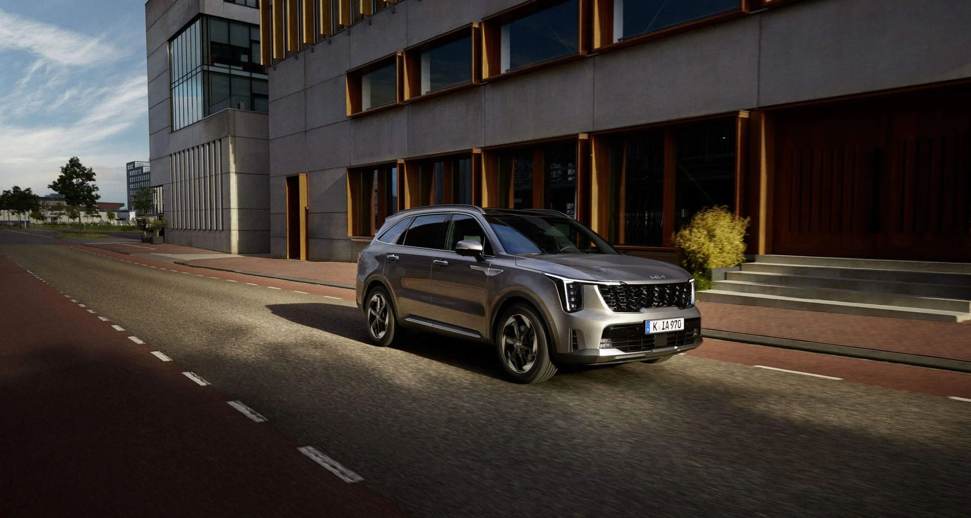 Auto SUV di colore grigio che percorre una strada cittadina con edifici moderni sullo sfondo