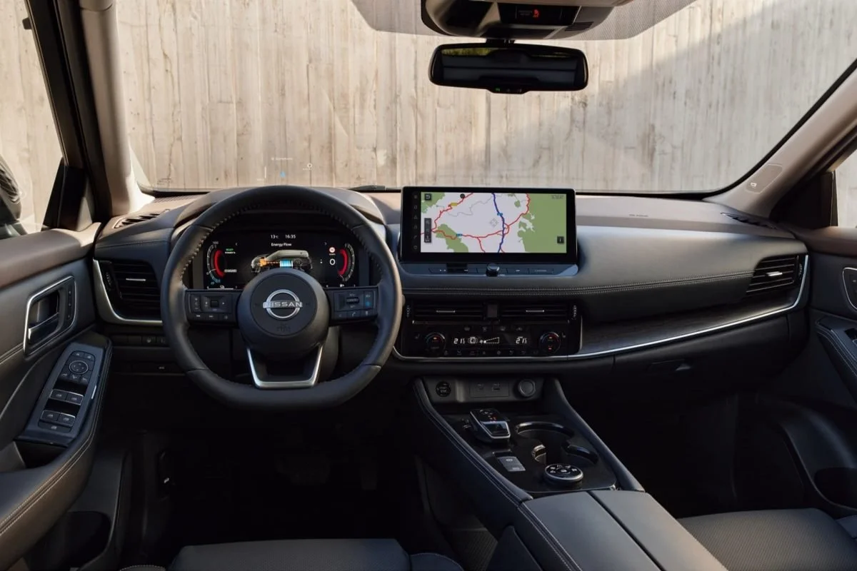 Interno di un'auto Nissan con volante, schermo di navigazione e pannello di controllo centrale.