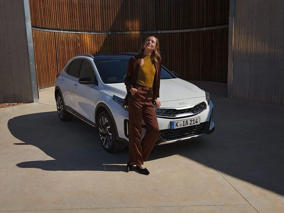 Donna che posa davanti a un'auto bianca in un'area aperta con pareti di legno.