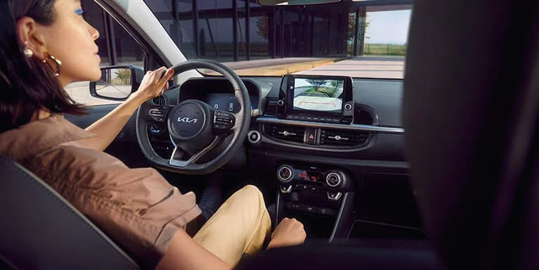 Interno di un'auto con una donna al volante, cruscotto con display digitale e schermo centrale per il sistema di navigazione.