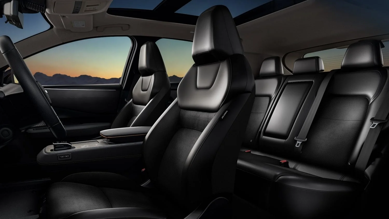 Interno di un'auto con sedili in pelle nera, vista sul sedile anteriore e posteriore, al tramonto con montagne visibili attraverso i finestrini.