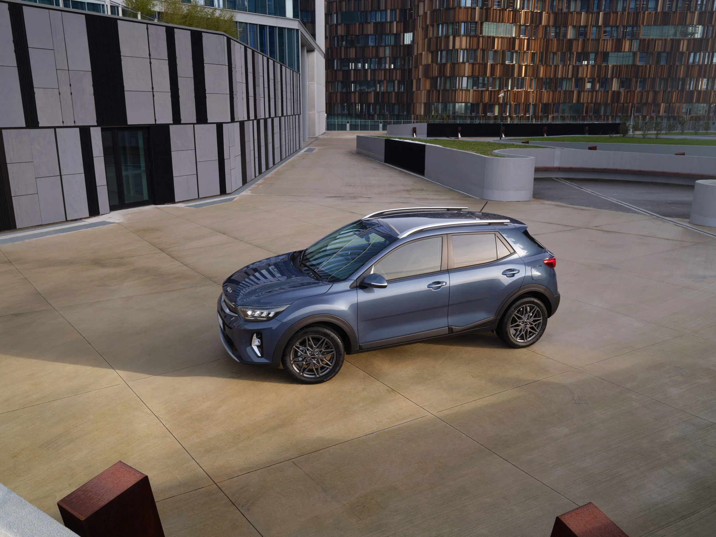 Auto sportivo blu in un parcheggio di cemento, con edifici moderni sullo sfondo.