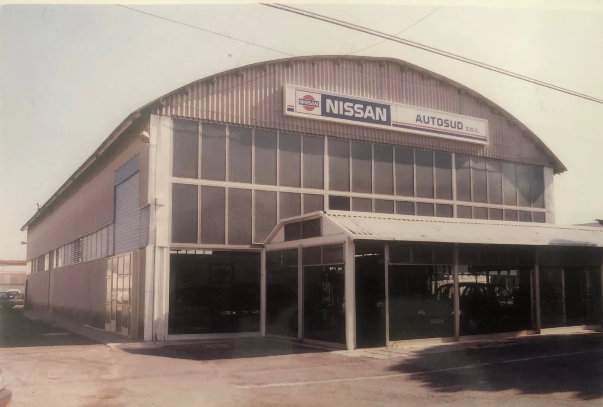 Edificio con segnale NISSAN e AUTOSUD s.n.c., struttura in metallo e vetro, parcheggio frontale