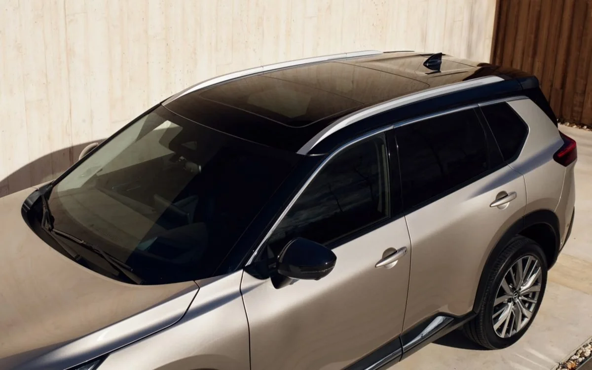 Auto SUV di colore beige e nero con tetto in vetro panoramico, parcheggiata in un cortile.