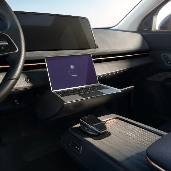 Interno di un'auto con laptop, smartphone e schermo digitale del veicolo.