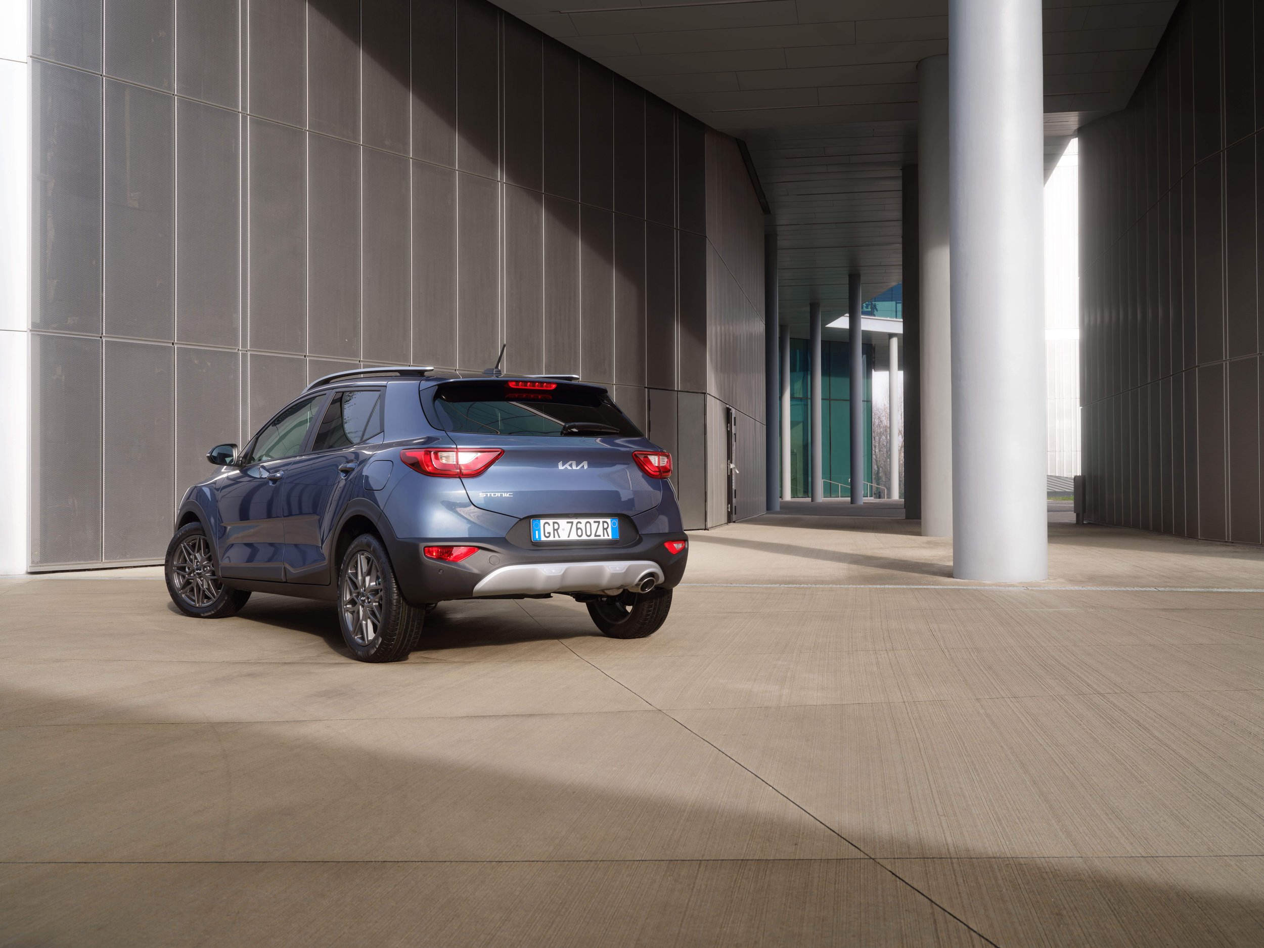 Auto compatto blu parcheggiato in un'area moderna con pareti in metallo e colonne di supporto.