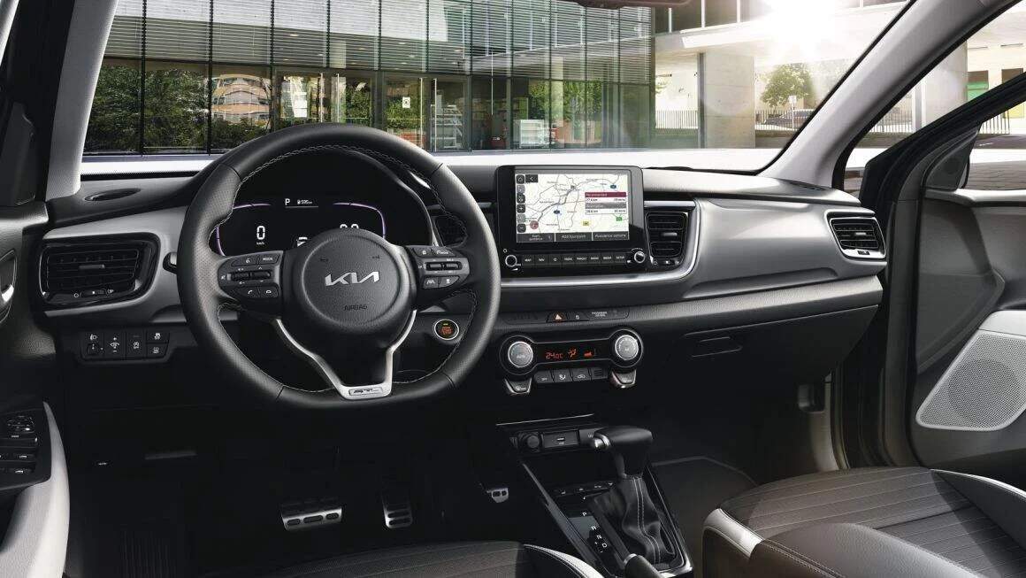 Interno di un'auto Kia con volante, display digitale, sistema di navigazione e controllo clima.