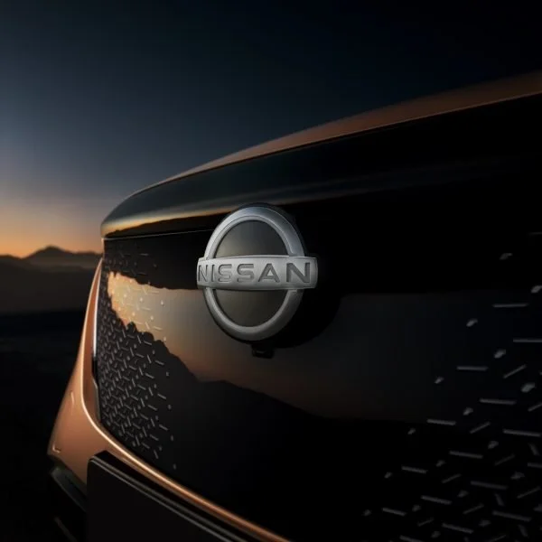 First planarte del logo Nissan su una vettura durante il tramonto, con sfondo di montagne e cielo scuro.