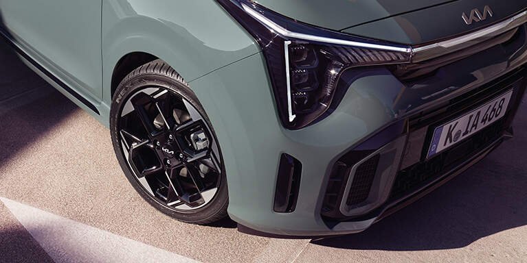 Particolare anteriore di una macchina verde con dettaglio di fari e ruota