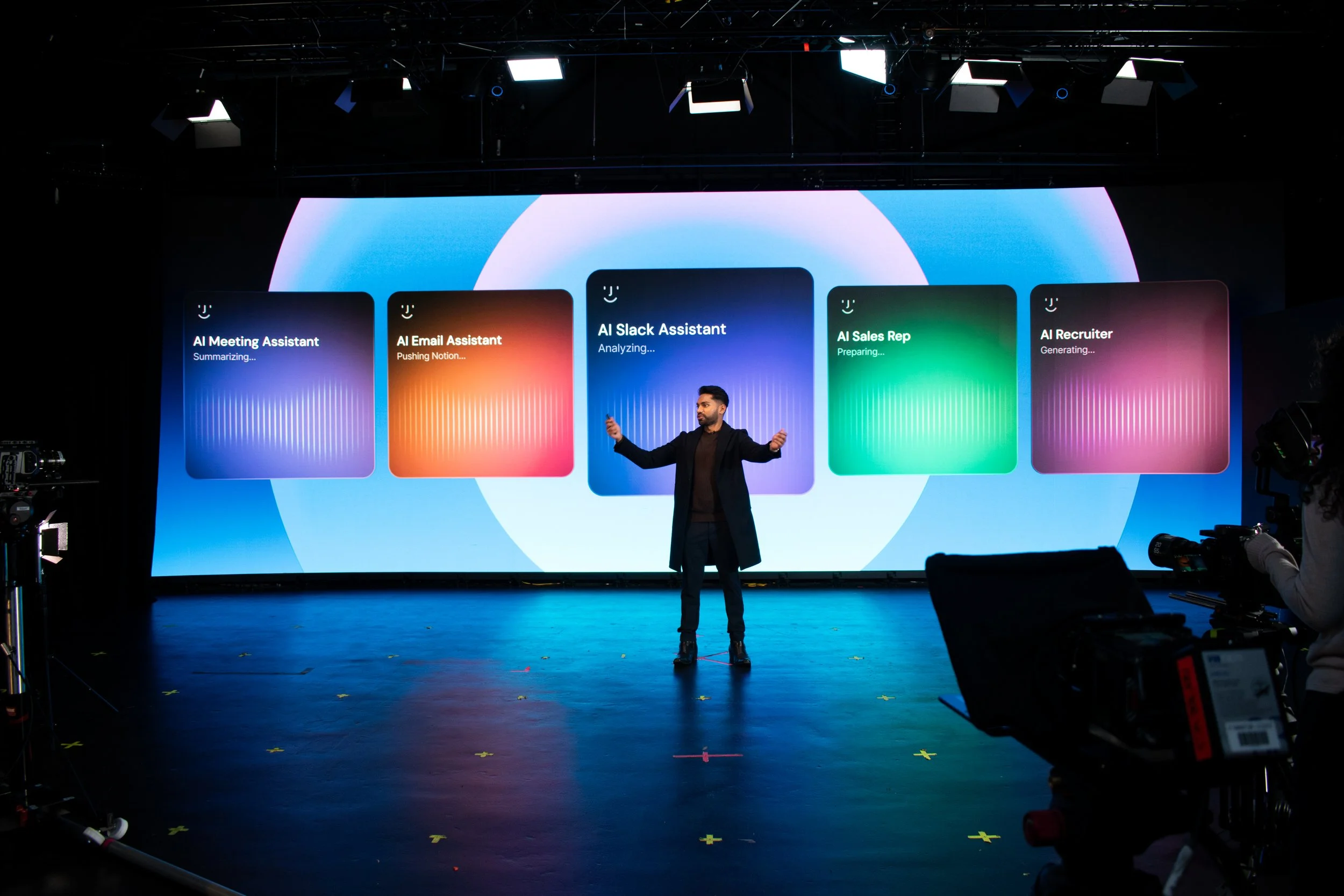 Presenter delivering a keynote-style talk on a virtual production stage, standing in front of a large LED wall displaying product features during a studio shoot.