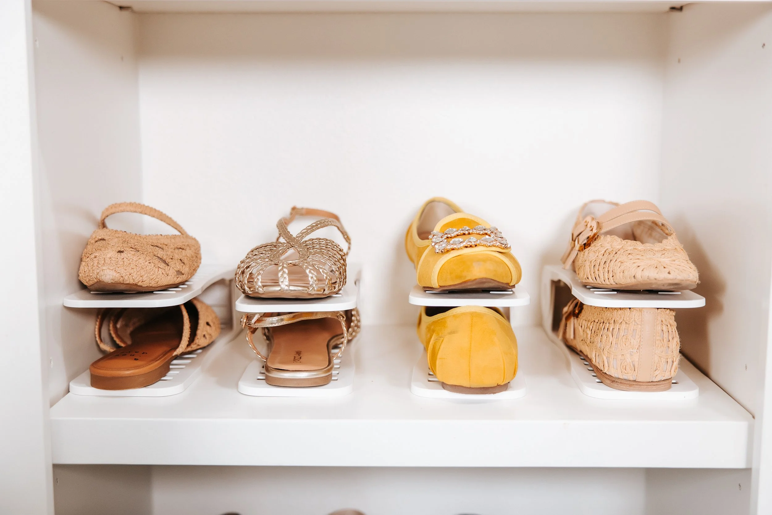 A white shoe rack inside a closet with six pairs of women's shoes, including sandals, heels, and wedges, in various colors and materials.