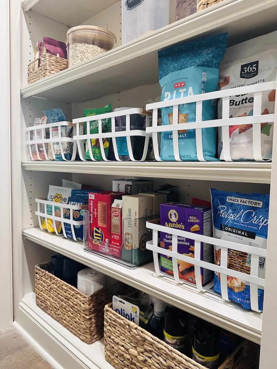 Pantry shelf with snacks, baked goods, and cleaning supplies in baskets.
