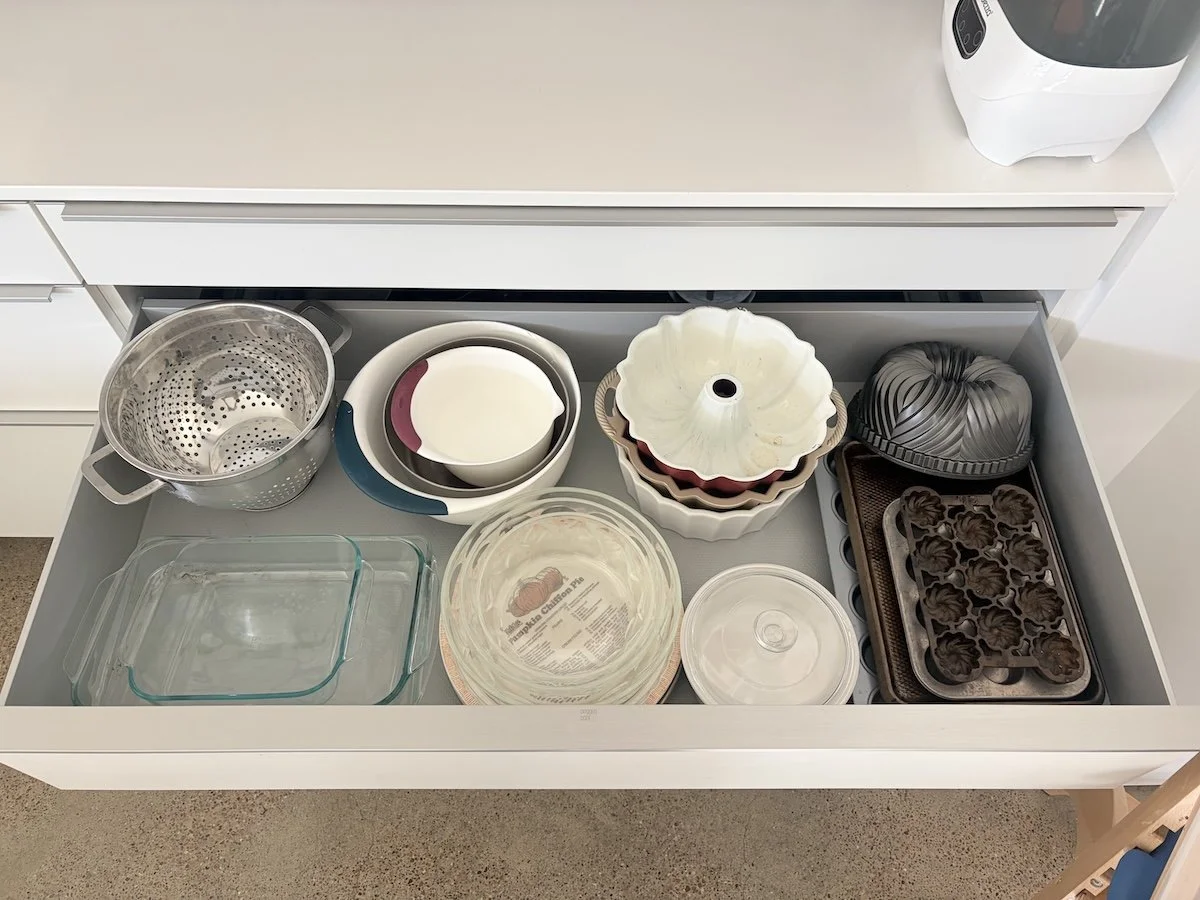 Kitchen drawer containing glass baking dishes, mixing bowls, cake pans, a silicone mold, a silicone heart-shaped mold, a metal muffin tin, and a metal steamer basket.