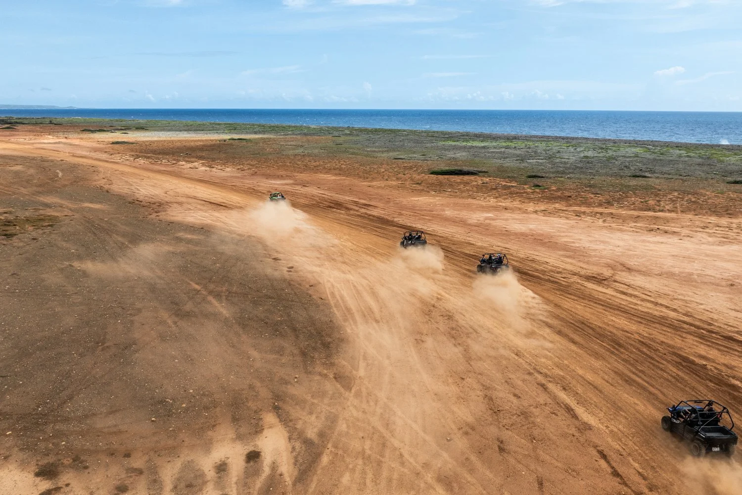 Buggy’s rijden over een stoffige kustvlakte op Curaçao, met de zee op de achtergrond.