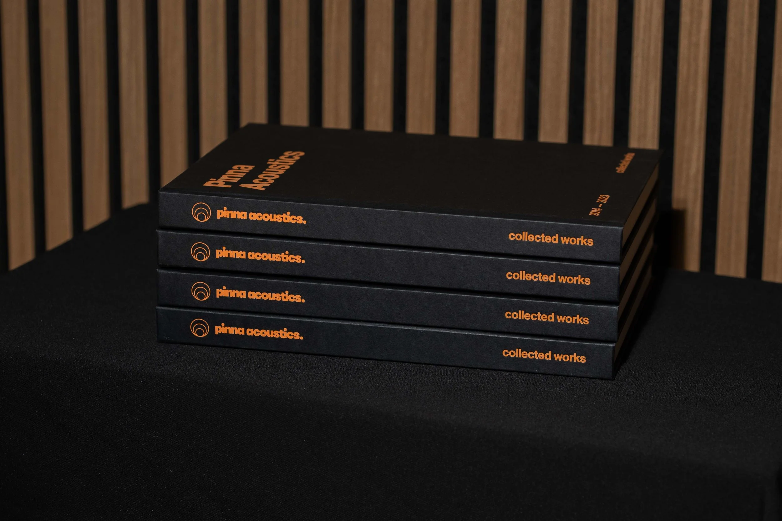 Stapel zwarte koffietafelboeken voor Pinna Acoustics met oranje typografie op de omslag en rug.