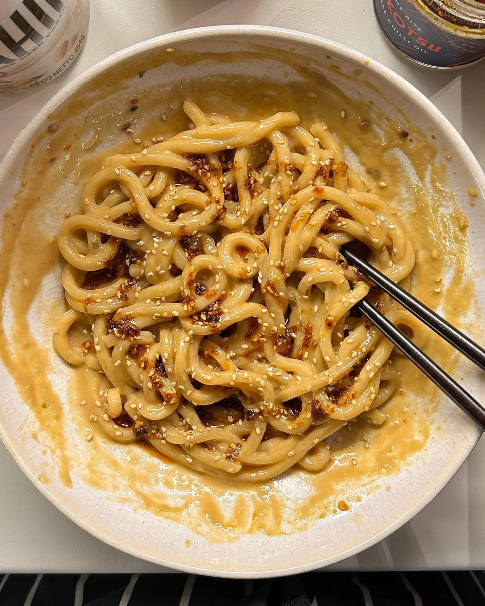 Saucy sesame noodles with chili oil and soy, with a pair of chopsticks sticking out and simple pantry ingredients surrounding.