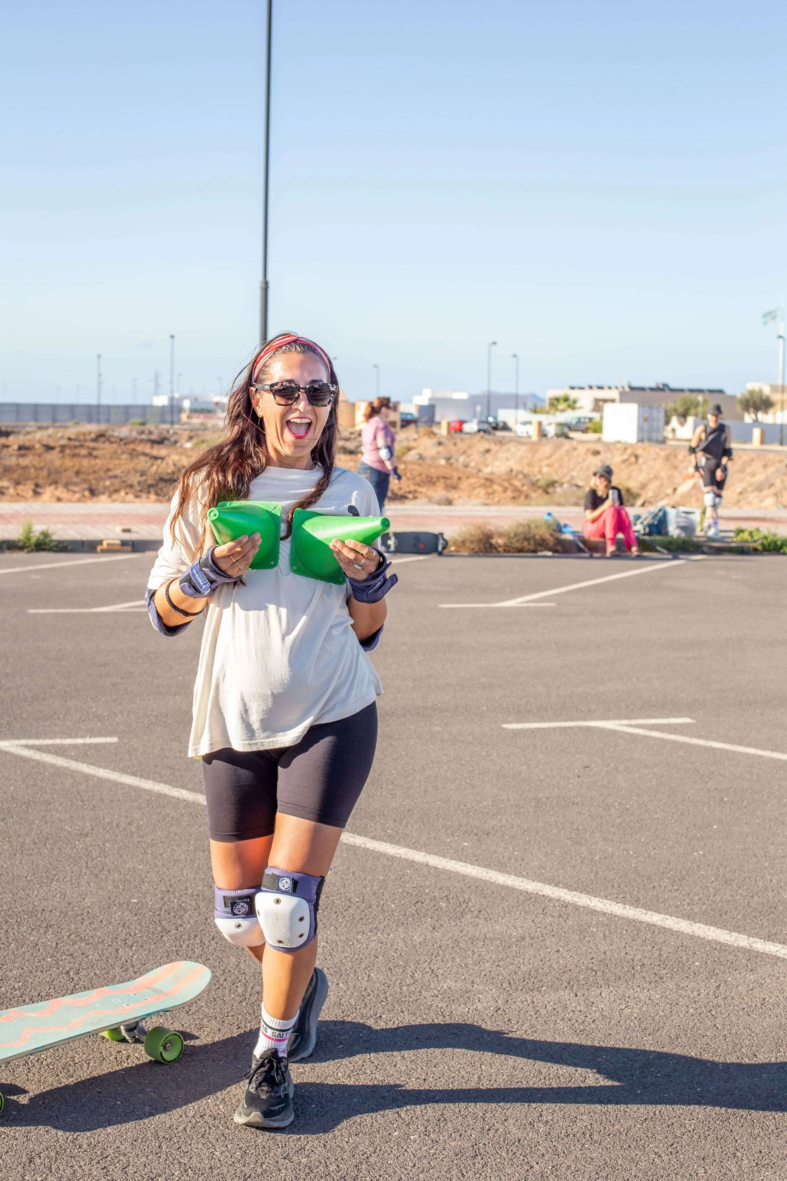 Woman in a blue rash guard surfing on a green surfboard in ocean waves, smiling and waving.
