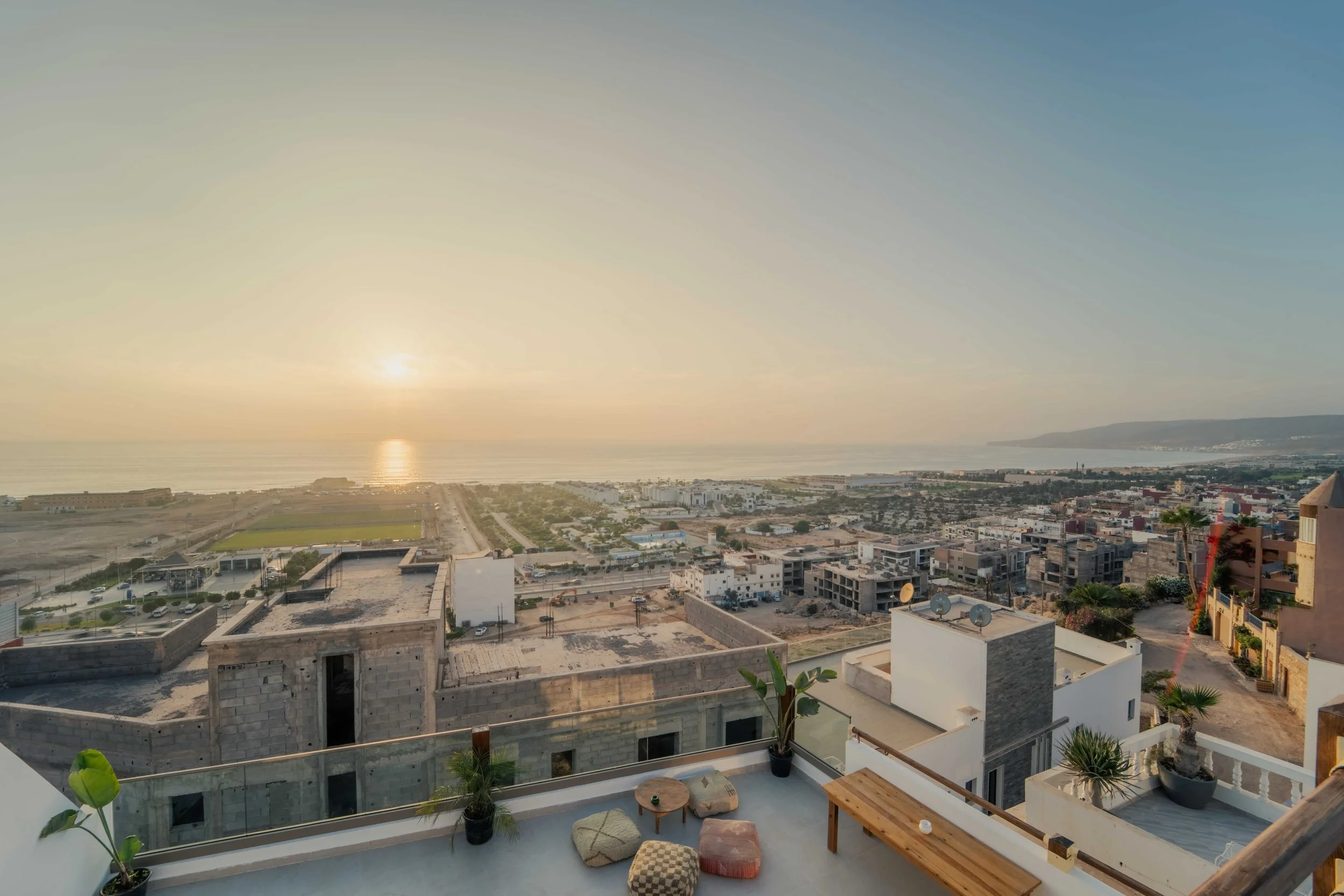 Sunset over a coastal city with buildings and an ocean in the background.