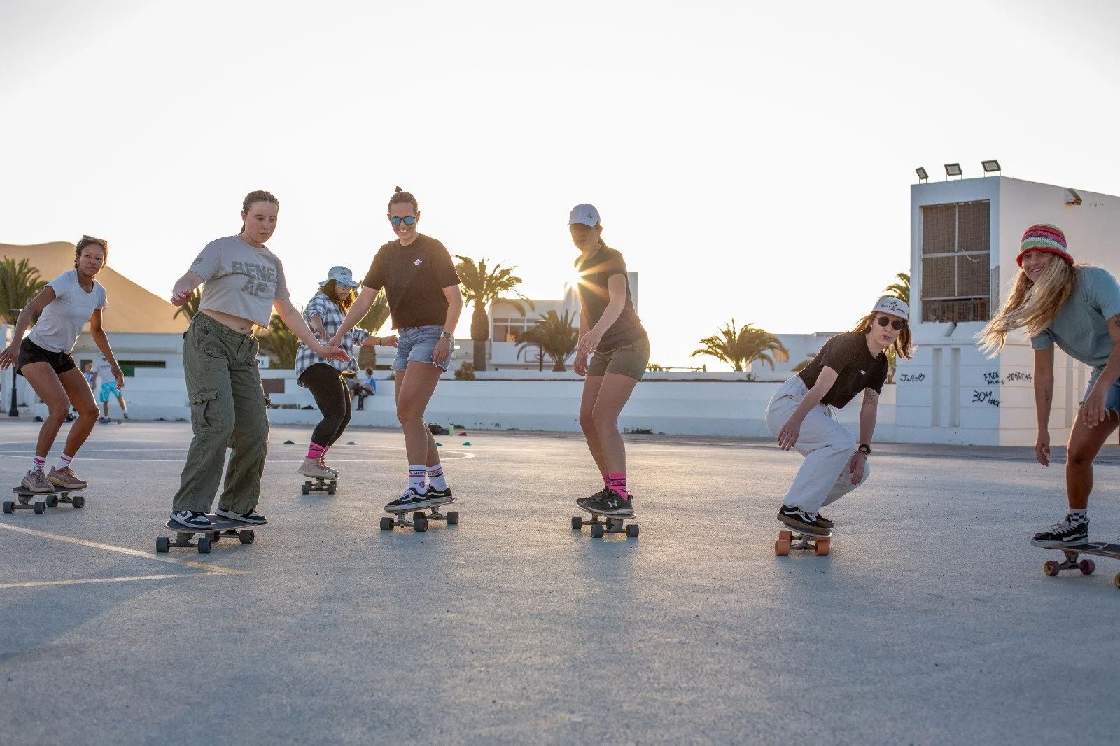 Four young women skateboarding on a street with palm trees and buildings in the background