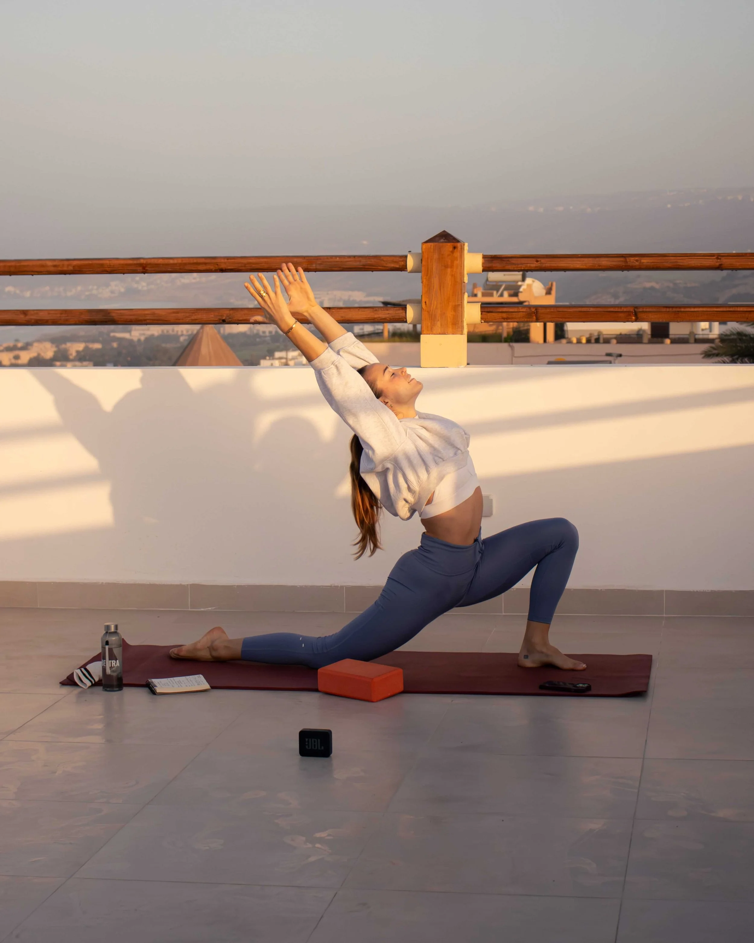 A group of women practicing yoga outdoors on a sandy surface, sitting in a kneeling meditation pose with eyes closed.