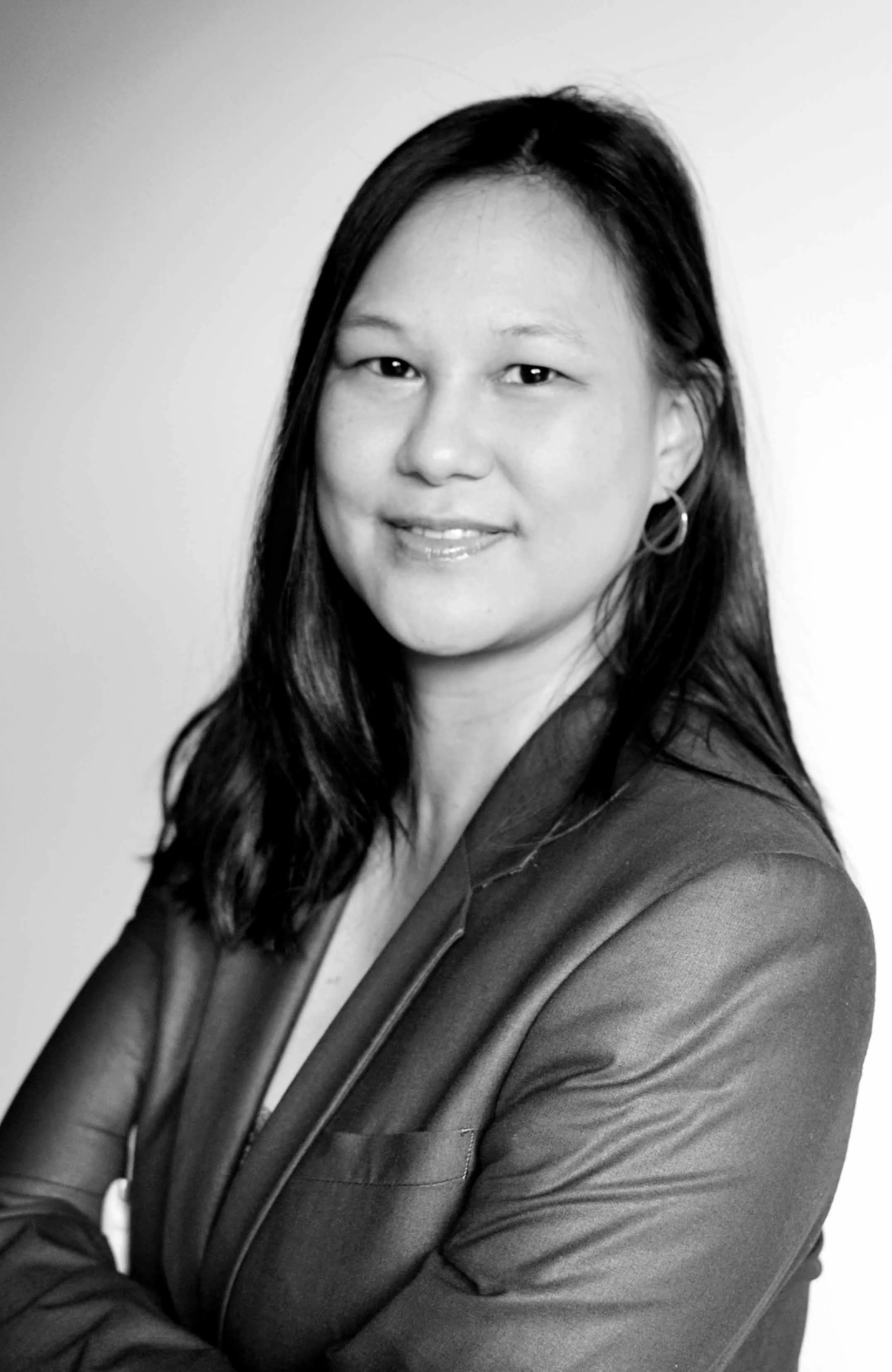 Portrait en noir et blanc d'une femme avec des cheveux longs, portant une veste en cuir, souriante, avec un fond clair.