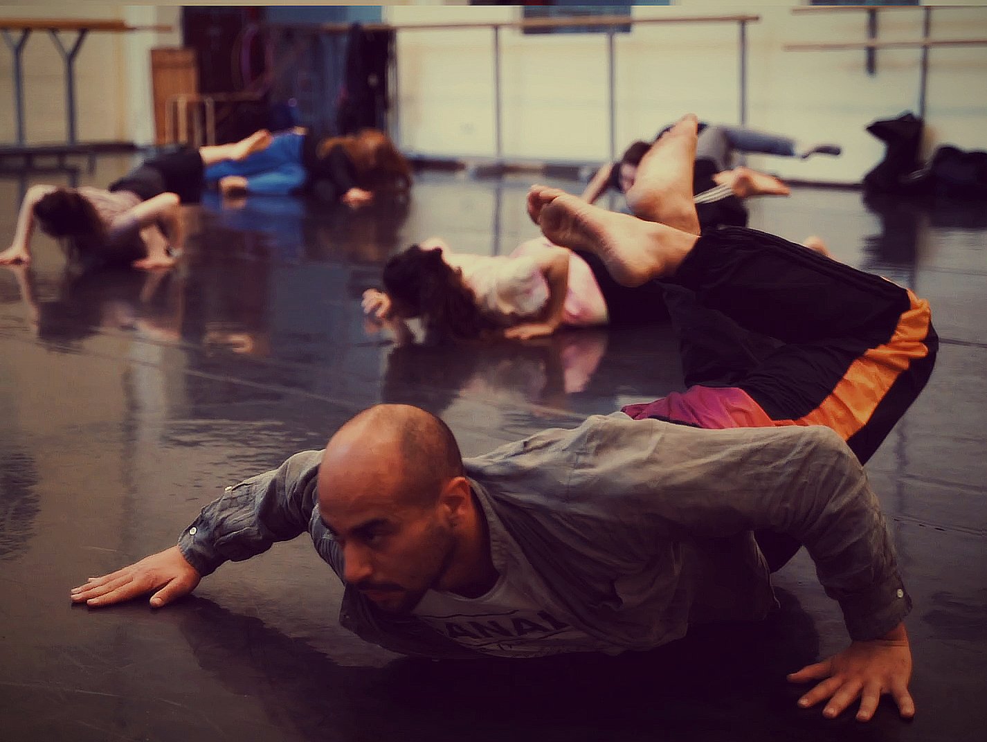 Niv Melamed, a man, in the midst of a floor work movement on the floor in a dance studio full of students