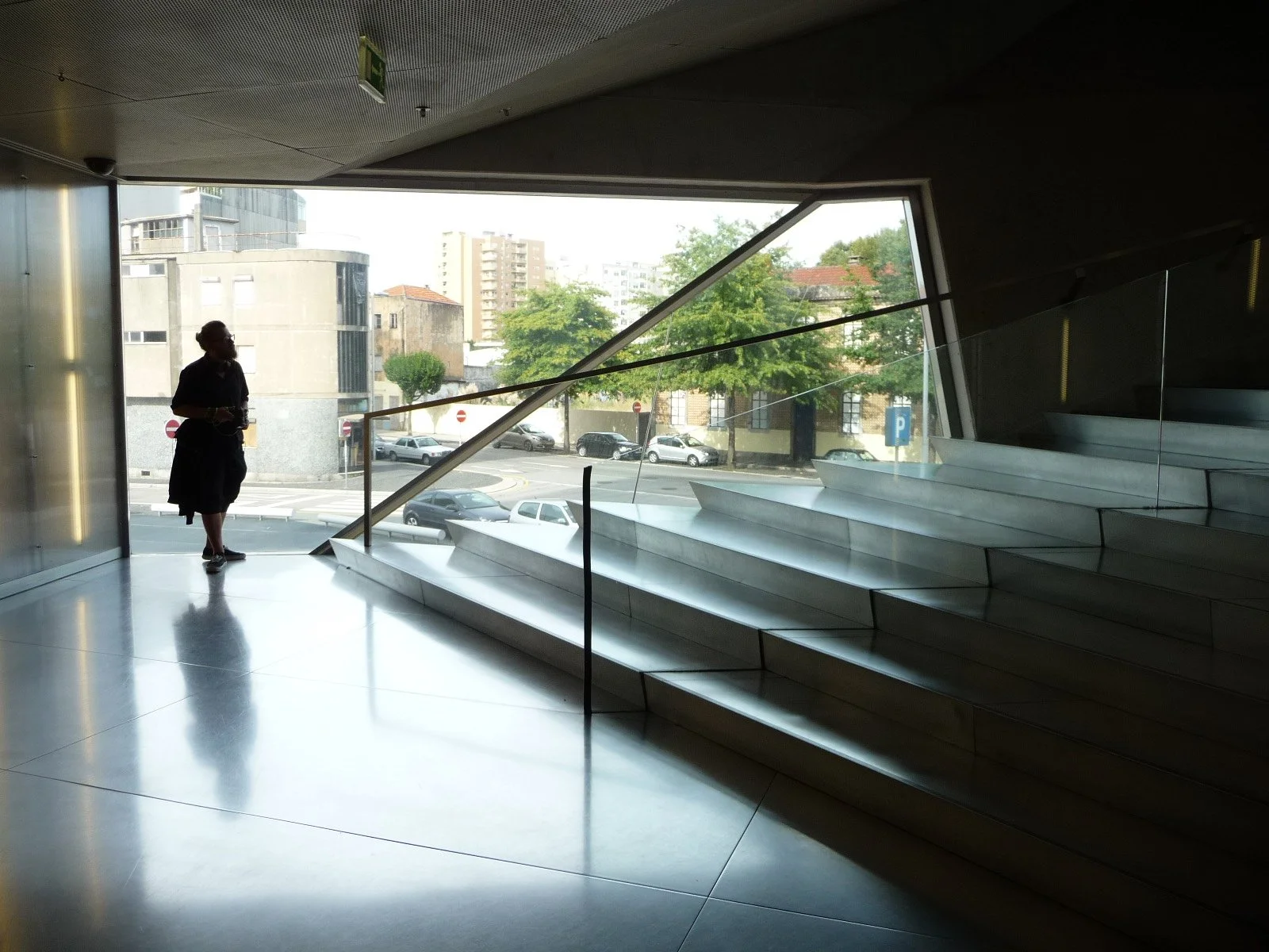 Une personne silhouette regarde à travers une grande fenêtre au-delà des escaliers en marbre dans un bâtiment moderne.