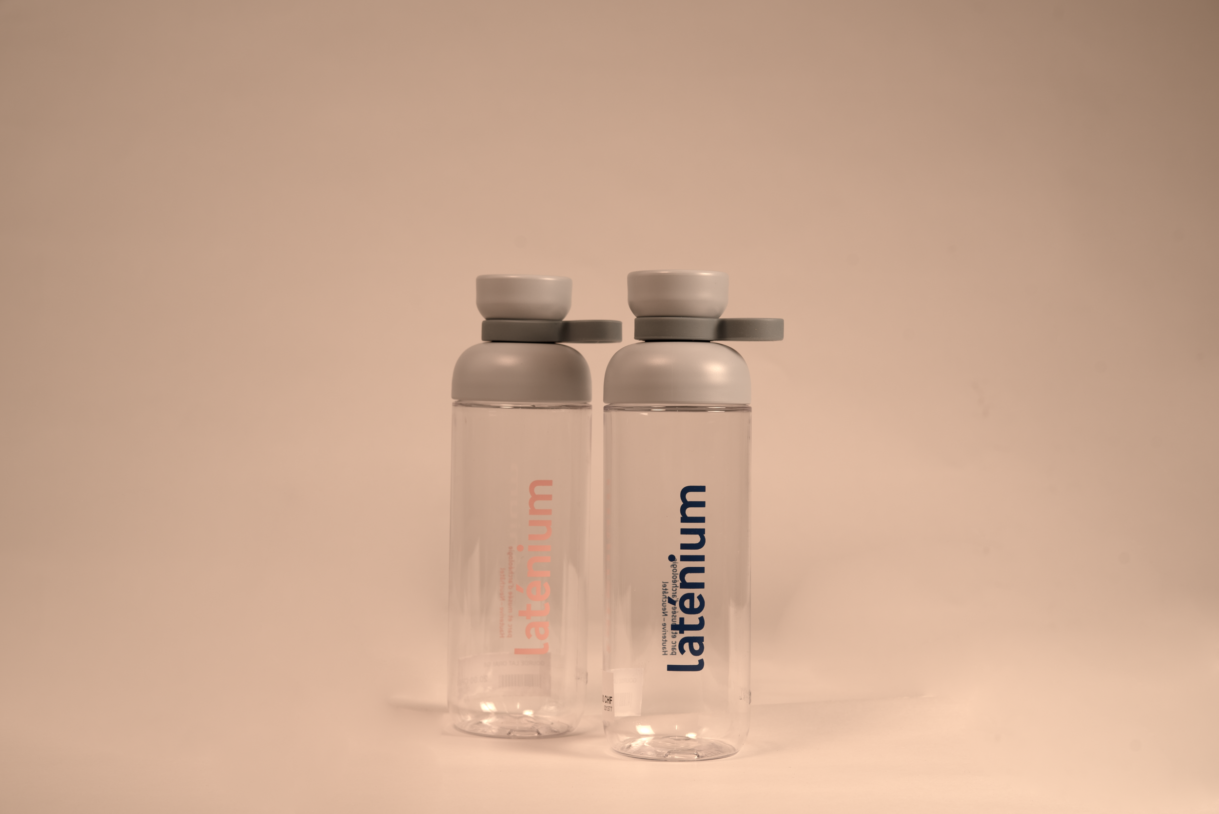 Deux bouteilles d'eau en plastique transparent avec bouchons gris, une portant la marque 'læténium' en rose et l'autre en bleu, sur un fond neutre.