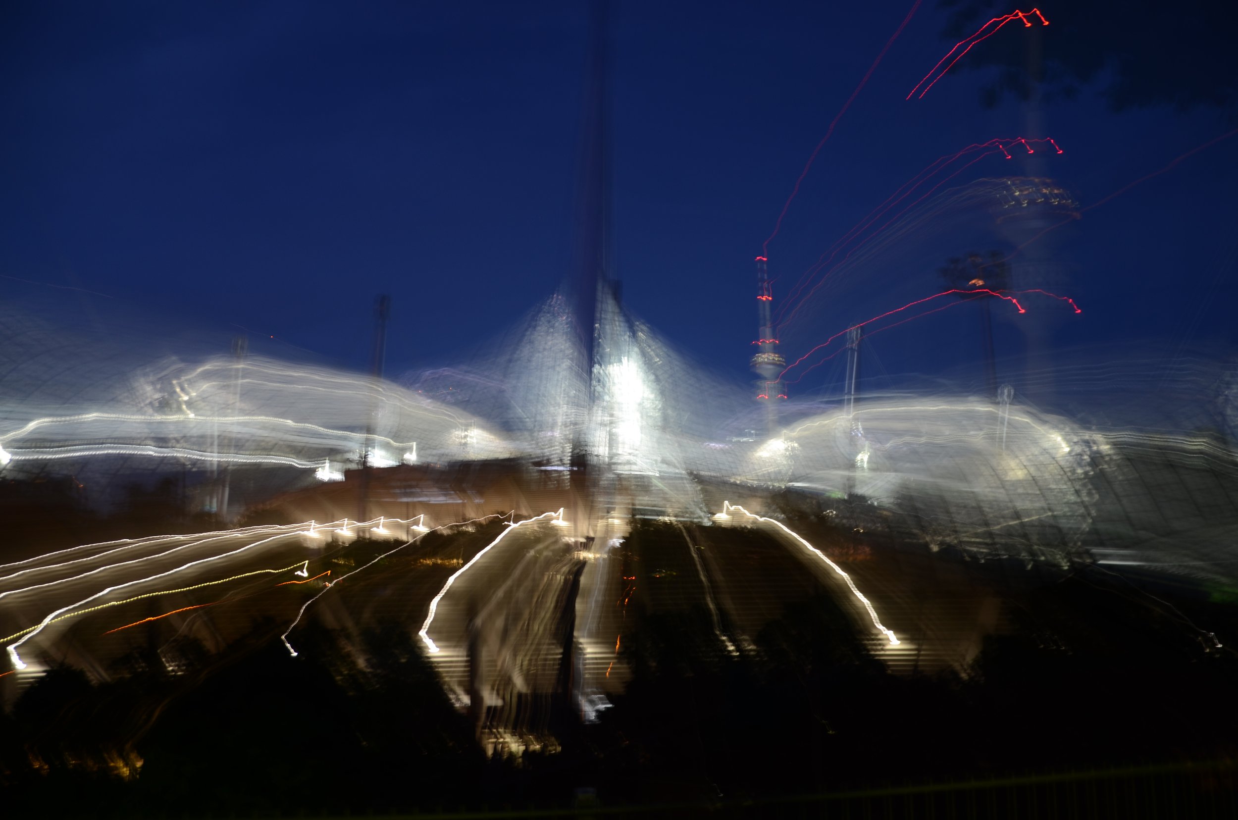 Photo nocturne d'une ville avec des lumières en mouvement, créant des tracés lumineux flous et des lignes d'étincelles dans le ciel.