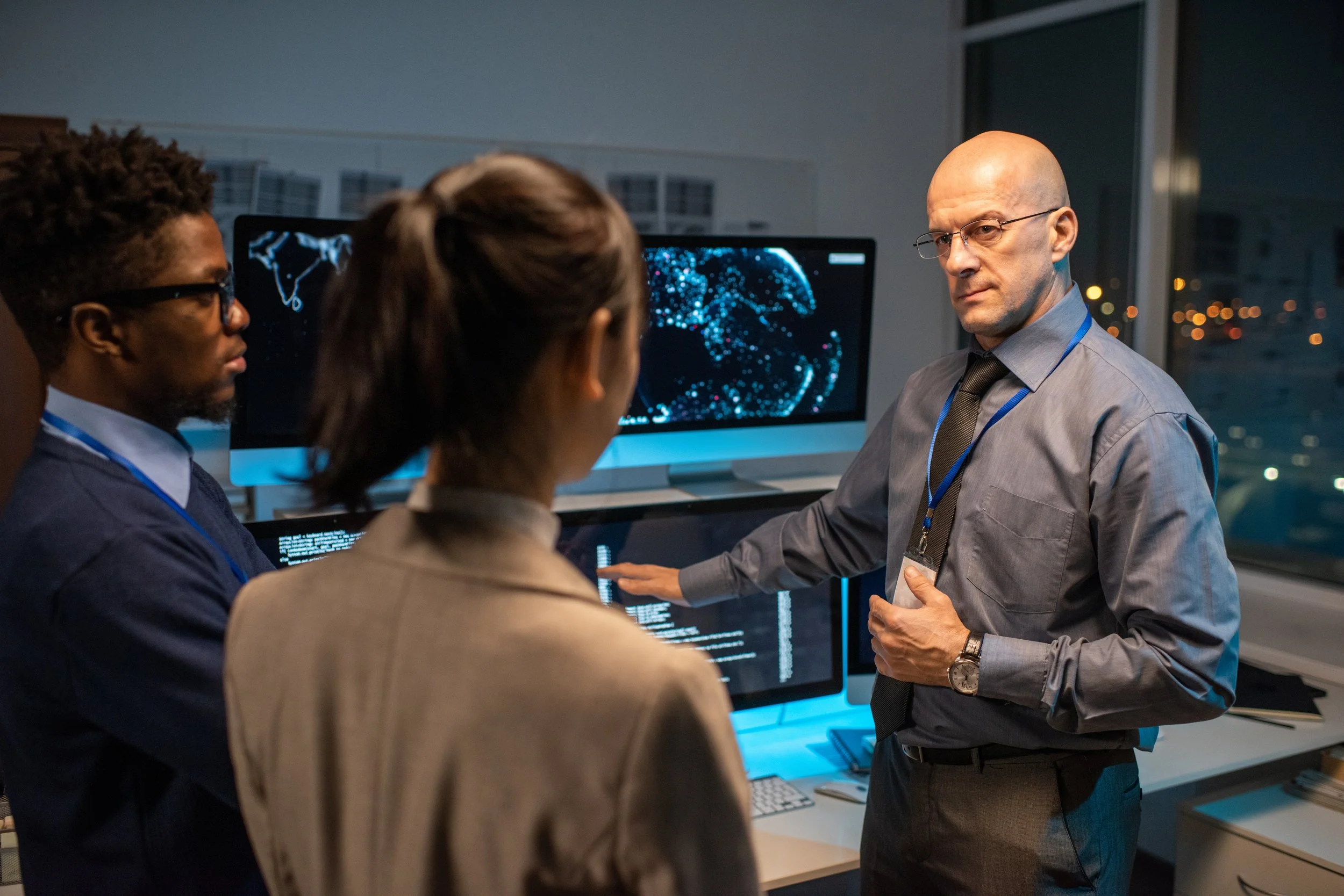 Picture of a cybersecurity team reviewing data on large digital monitors.