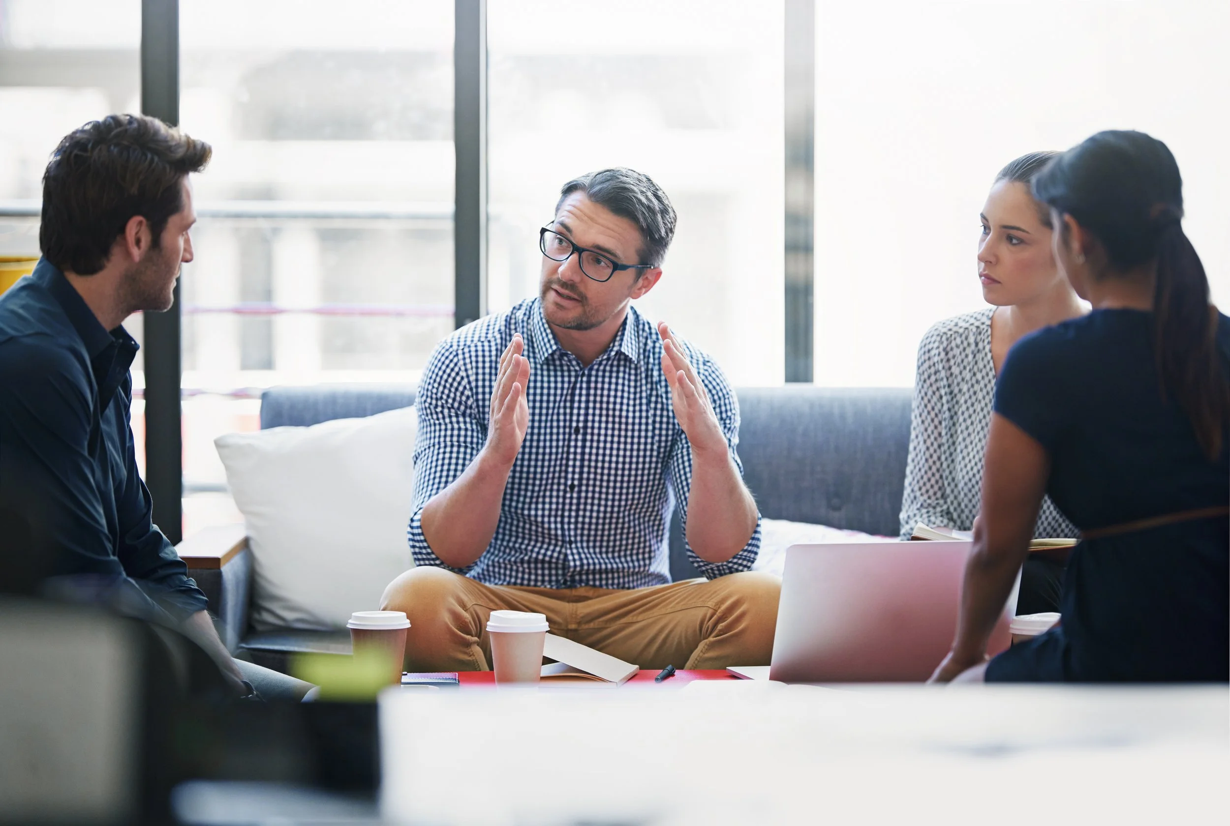 Picture of a small group having a discussion around a table with coffee cups and a laptop.