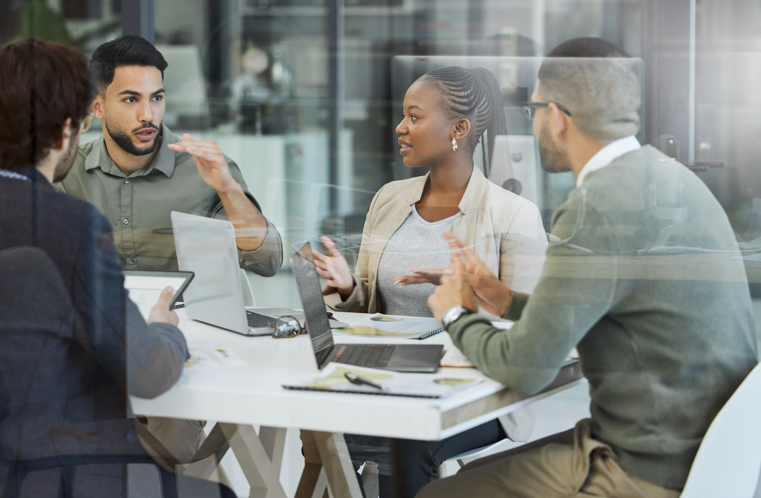 Picture of a team meeting around a table with laptops and documents.