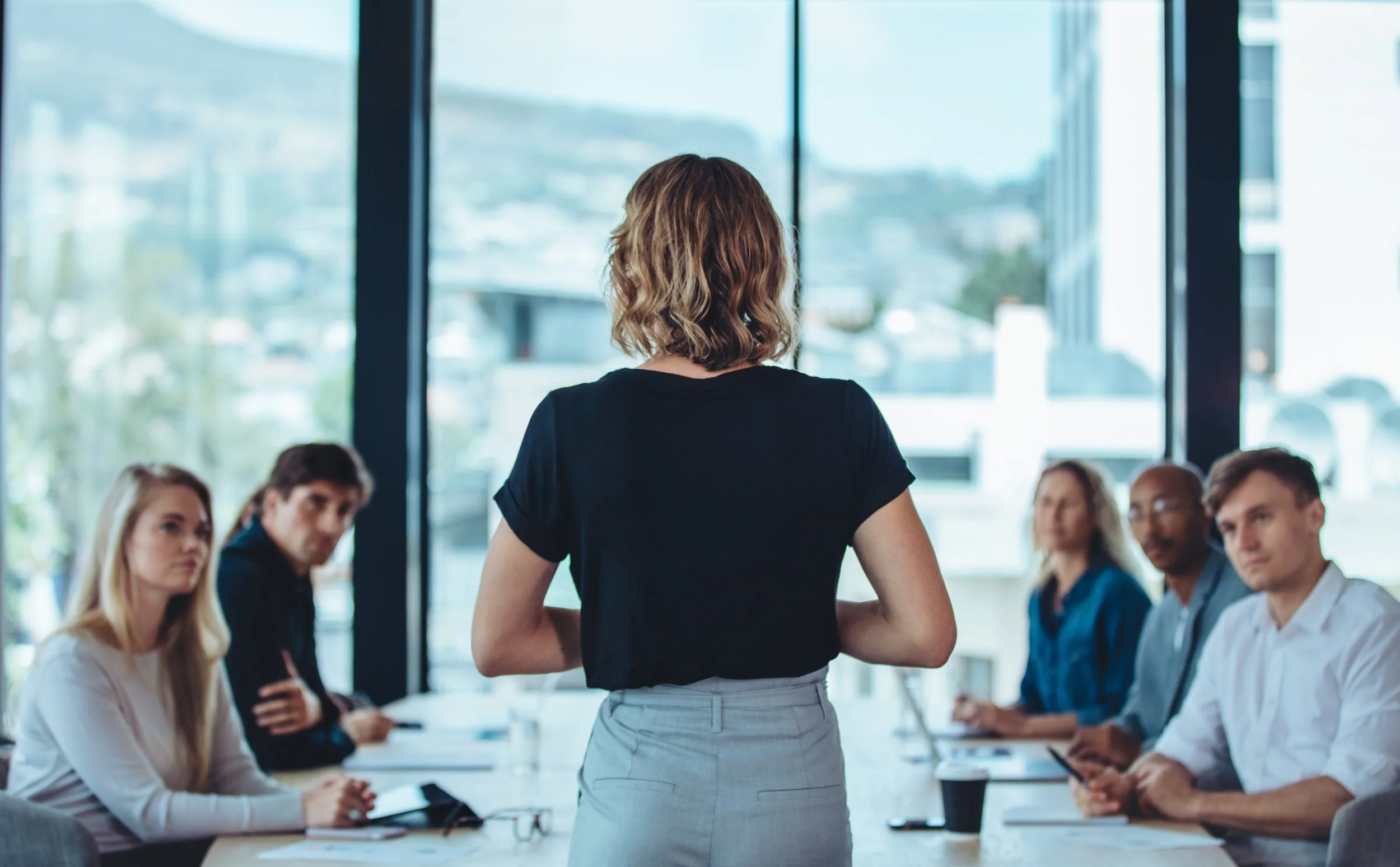 A picture of a presenter speaking to a team during a conference room meeting.