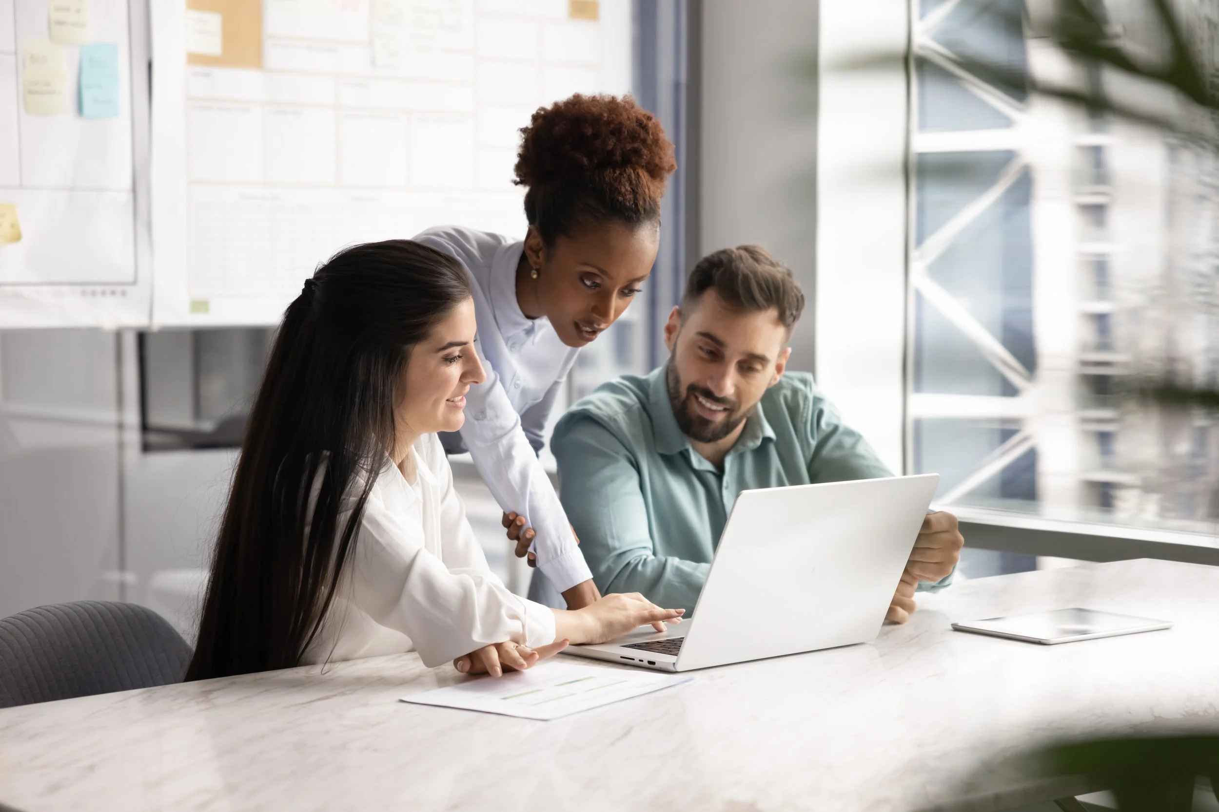 Picture of three coworkers collaborating around a laptop in a modern office.
