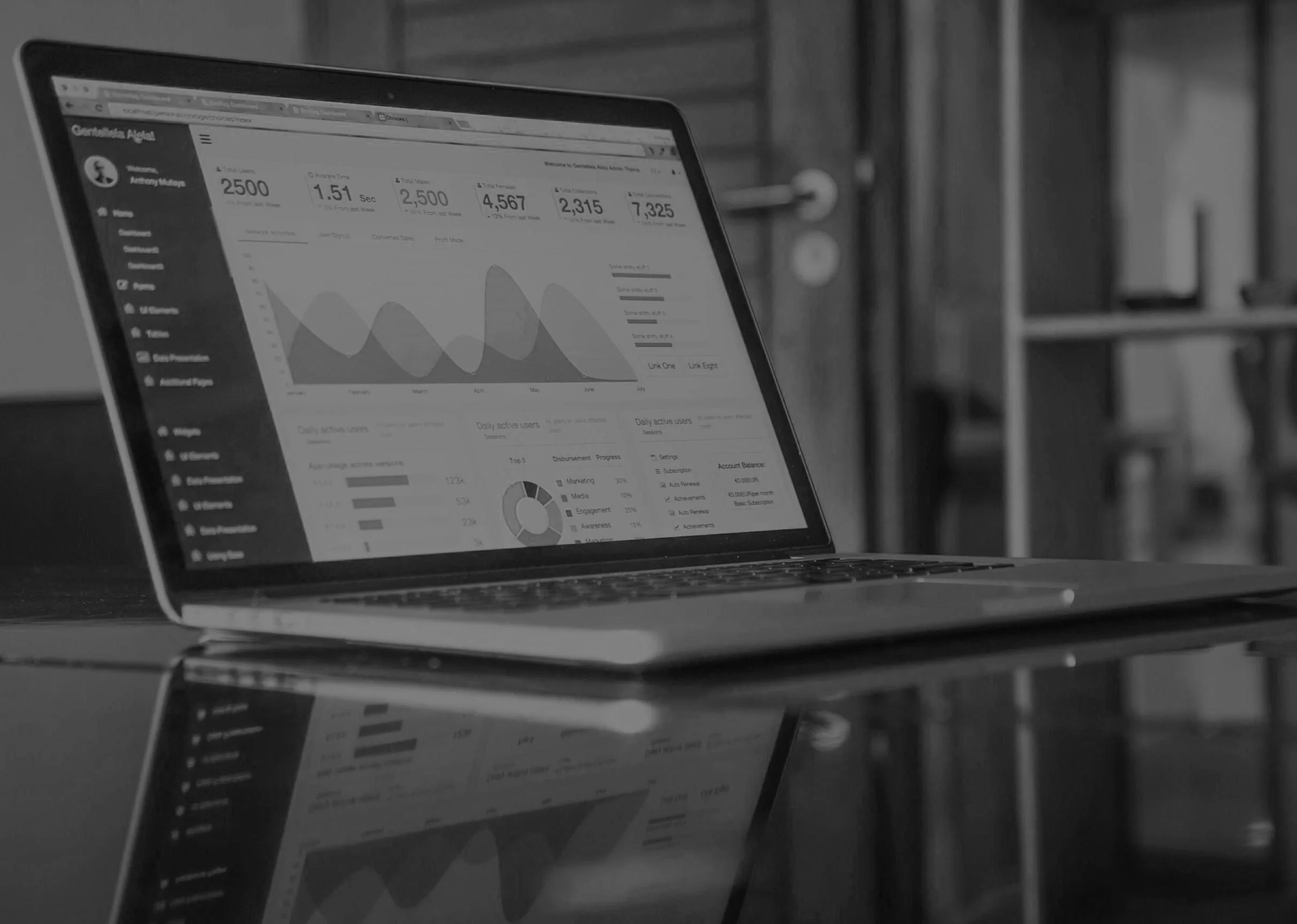 A laptop on a dark reflective surface displaying a dashboard with graphs and data analytics charts, in a modern office setting.