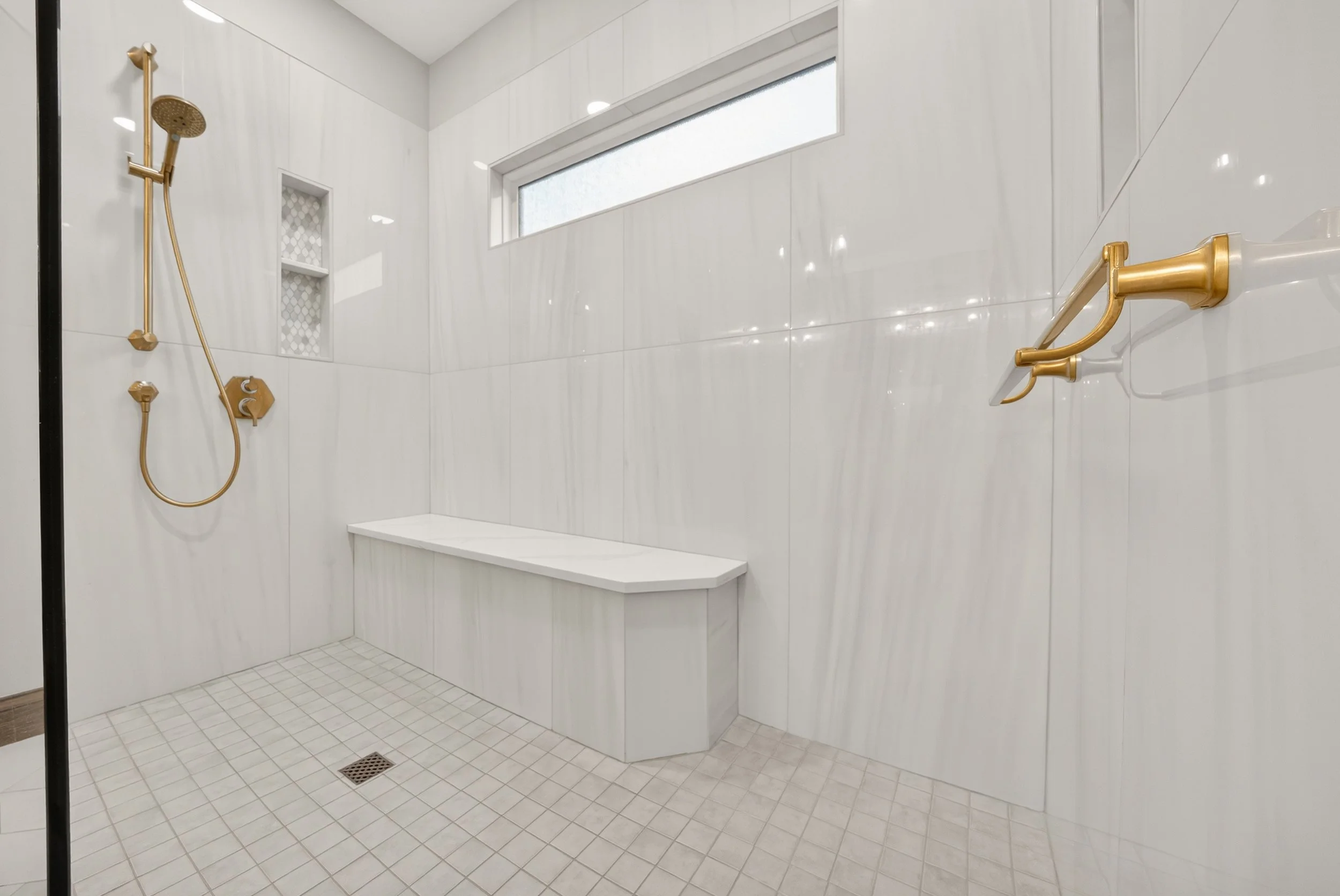 Curbless shower with natural tiling and gold accents showing a corner bench in the shower.