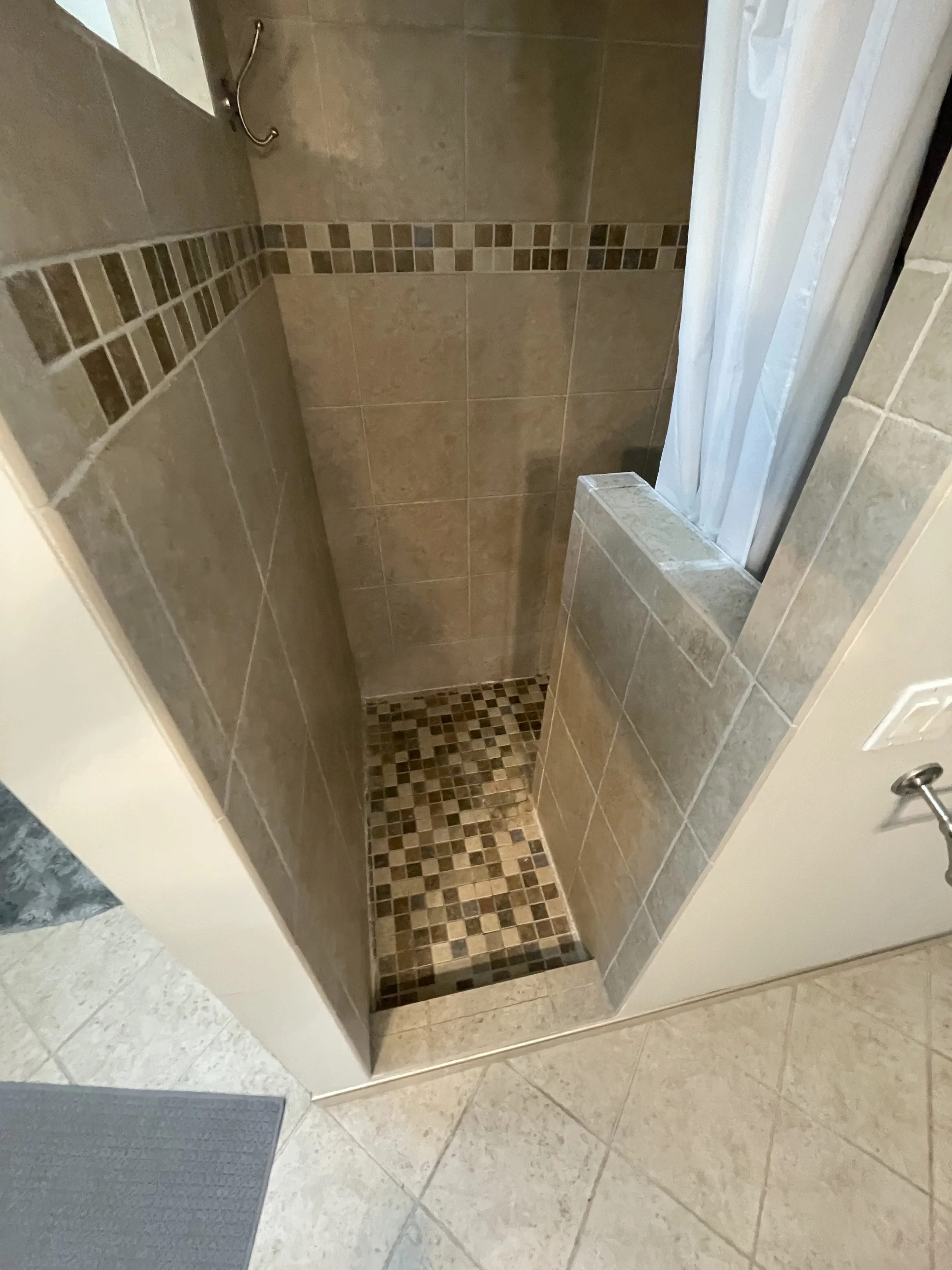 Built in beige tiled shower with mosaic floor