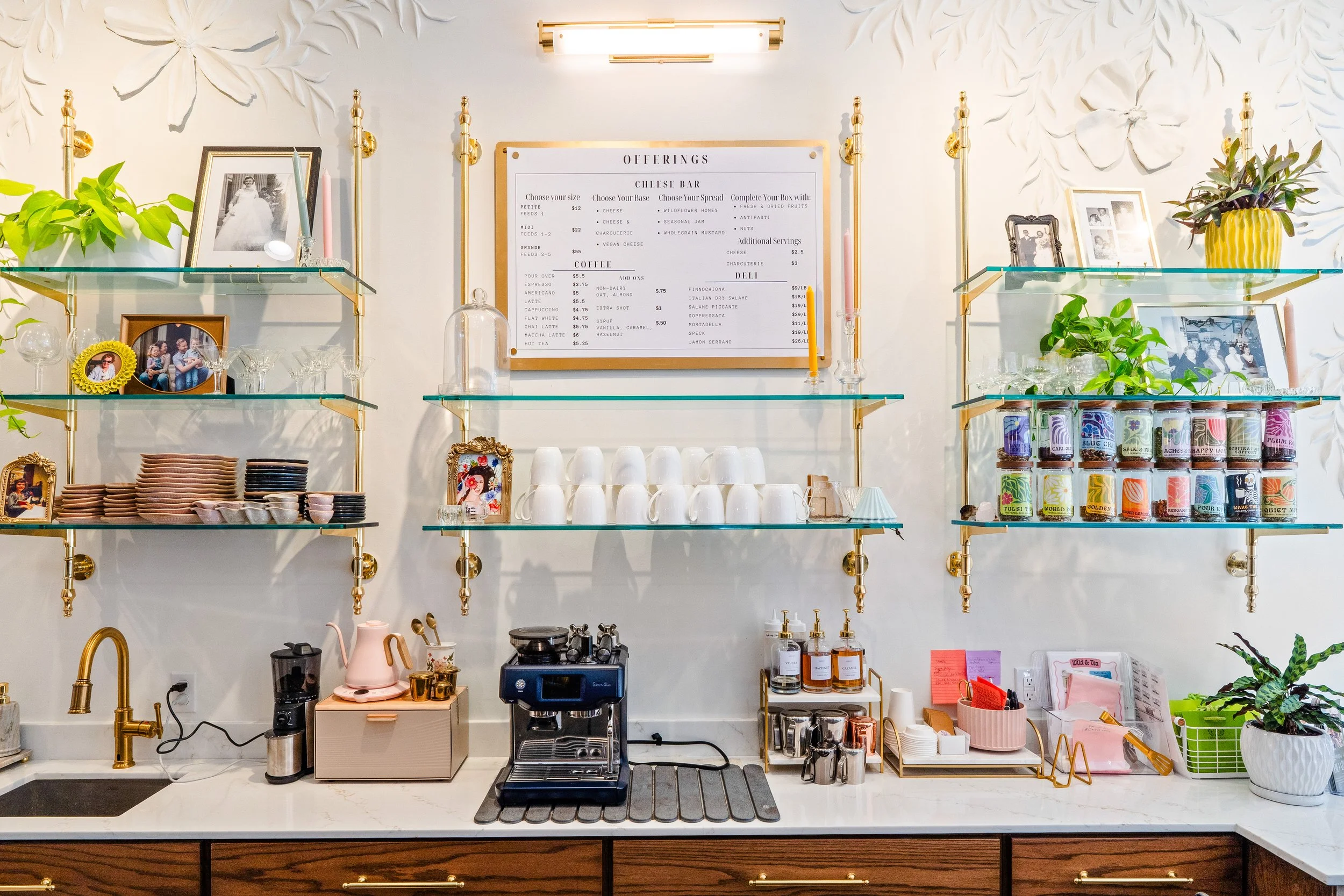 Cafe menu hung on wall above countertop with brass and glass shelving surrounding it.