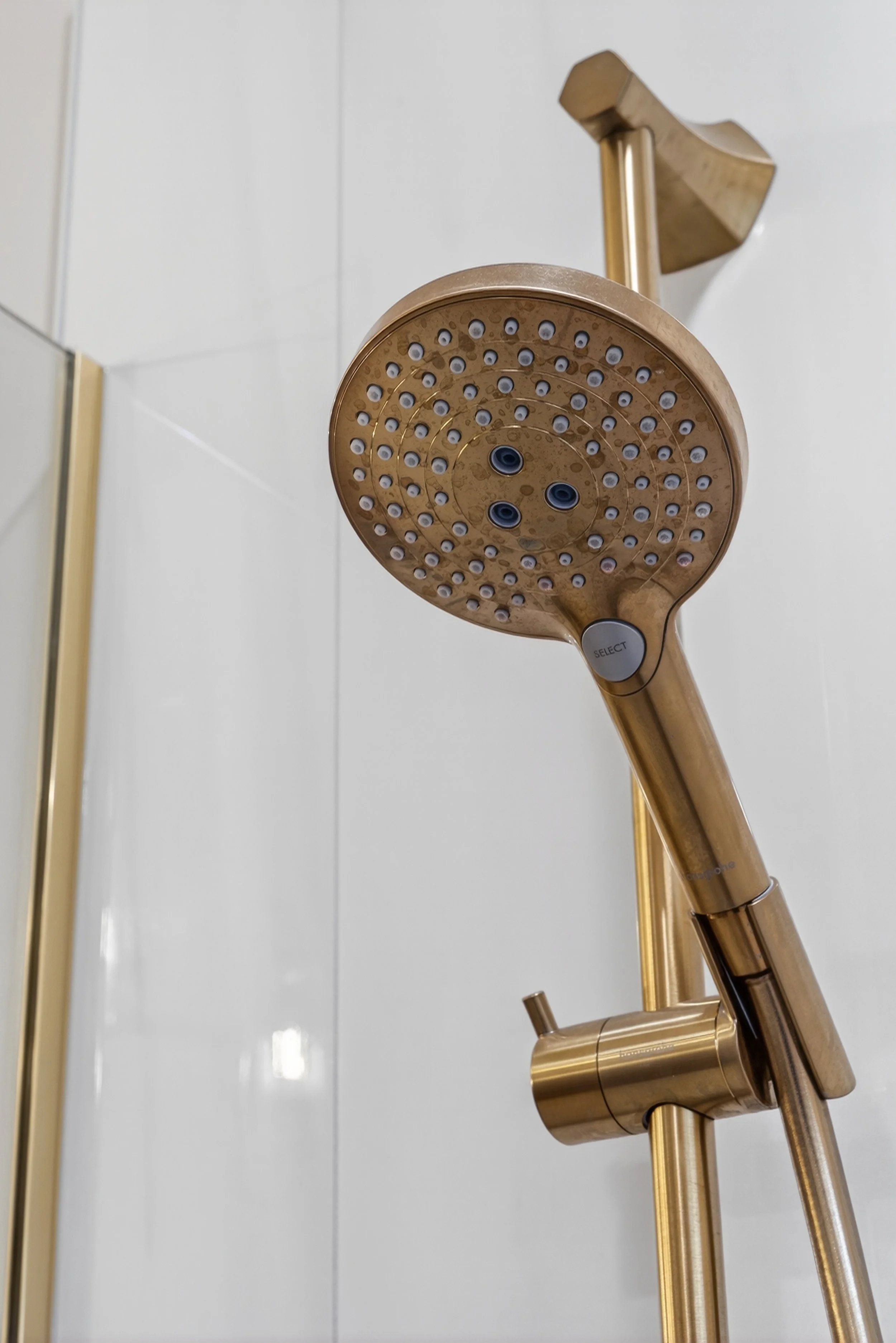 Handheld gold shower head on adjustment bar.