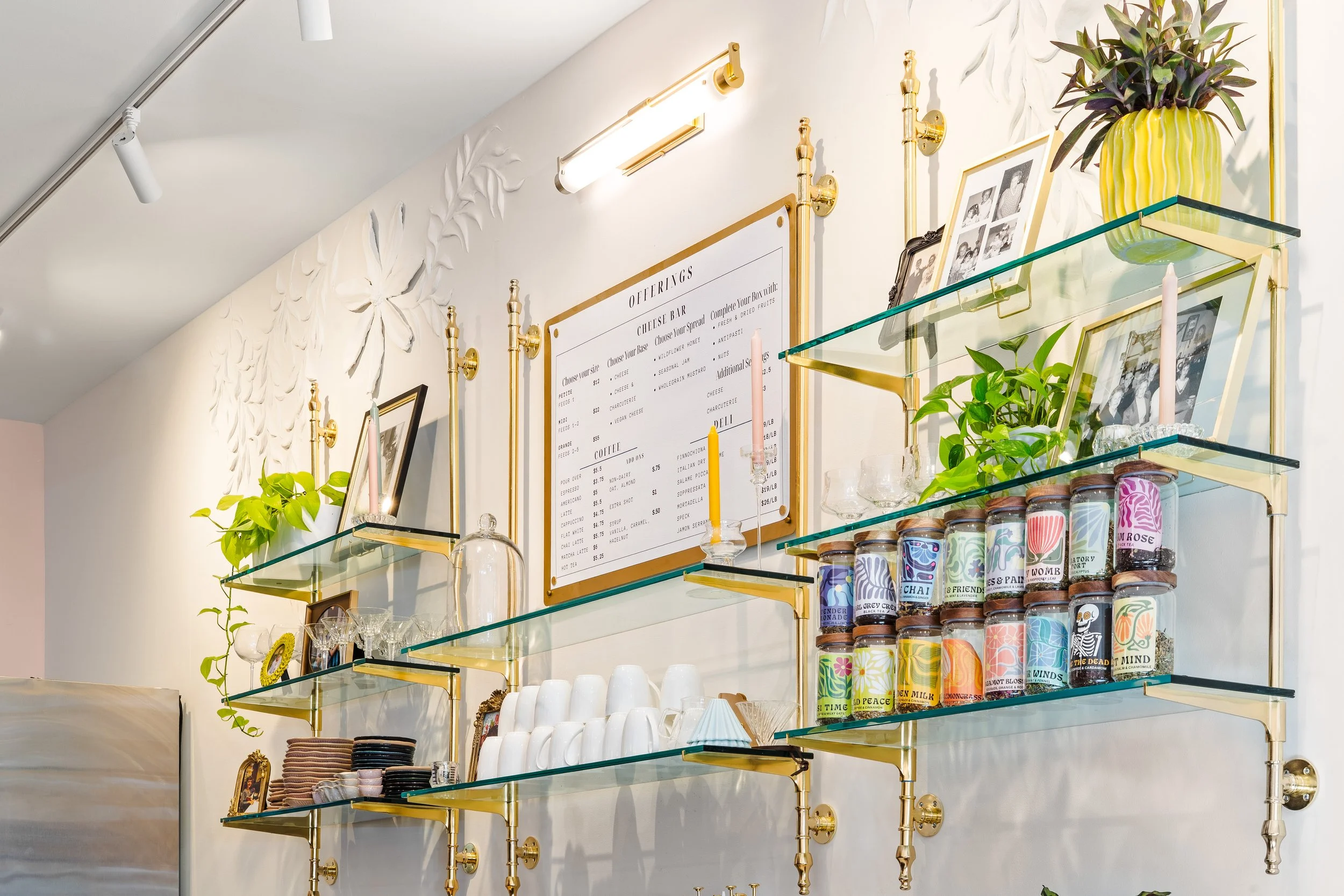 Cafe menu hung on wall with brass and glass shelving surrounding it.