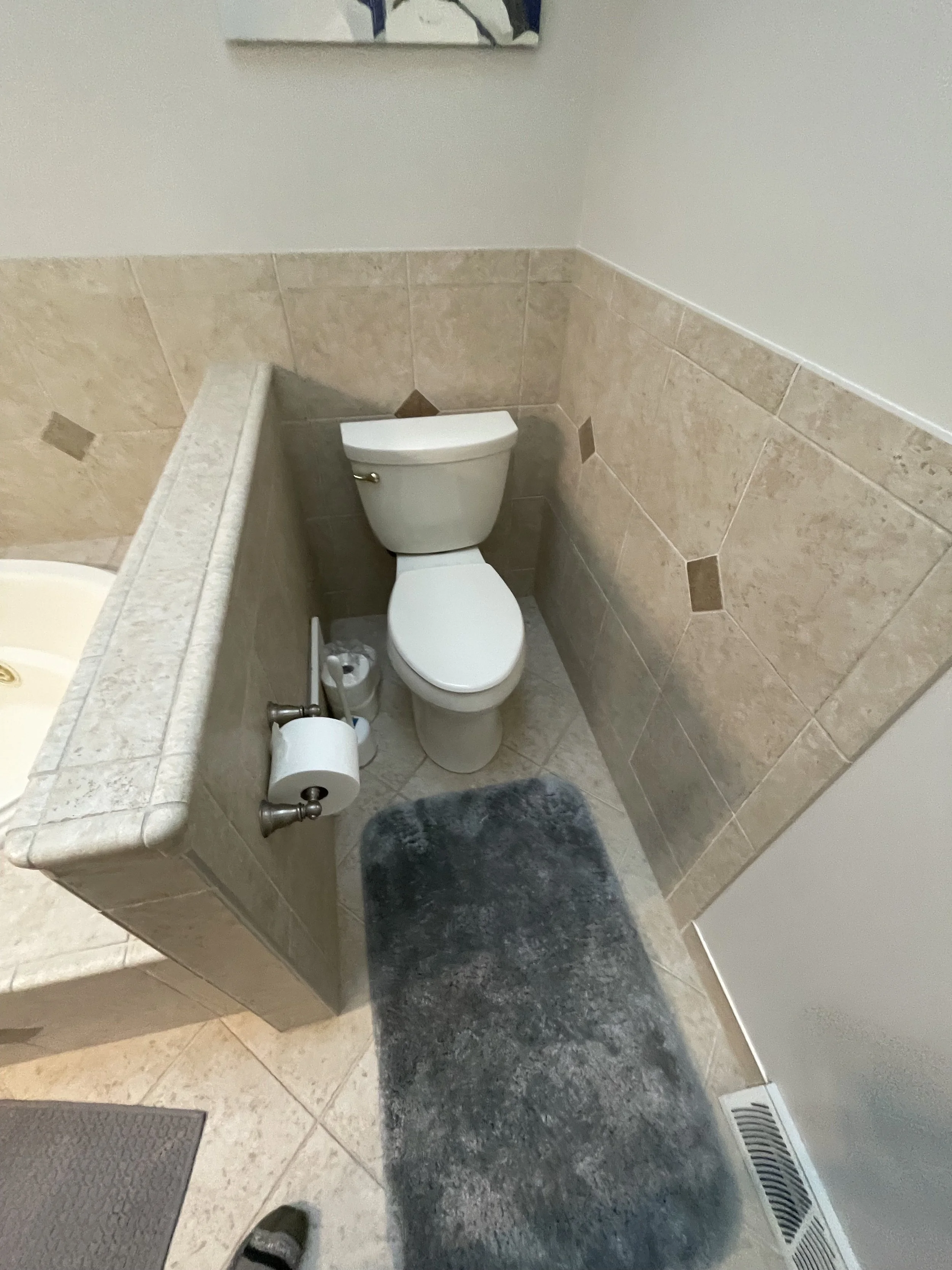 Toilet to the side of a beige tiled half wall