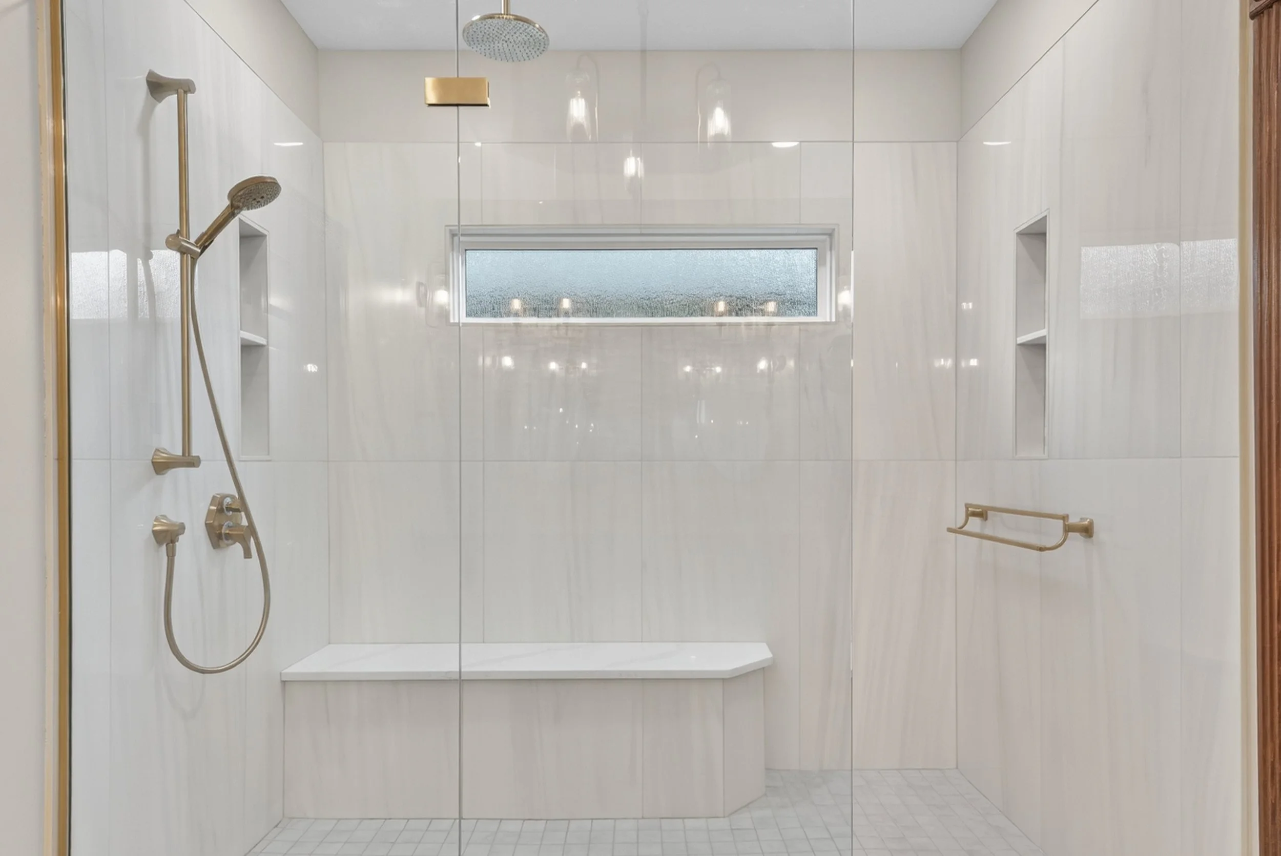 Curbless shower with glass door and a bench in the shower.