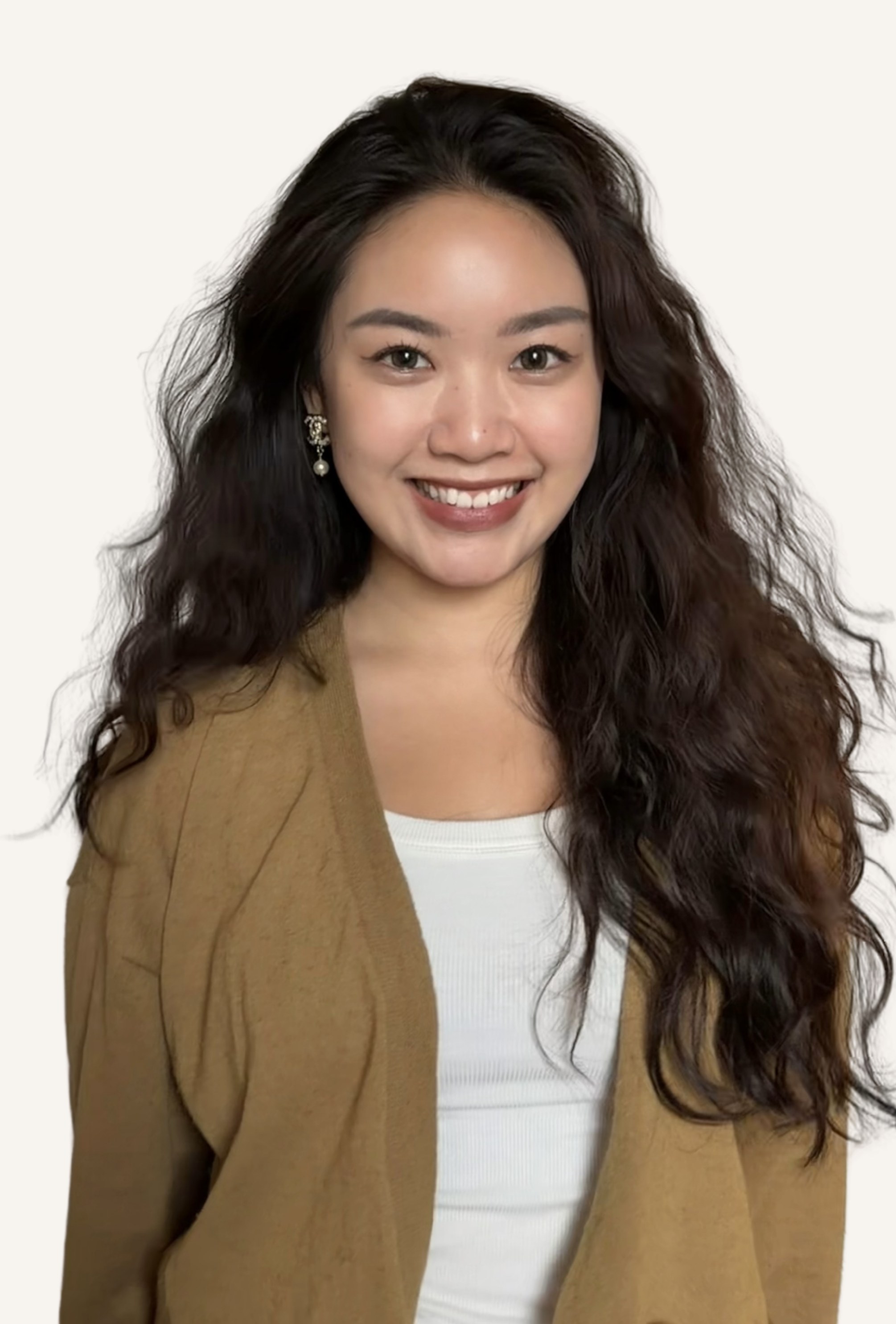 A smiling woman with long, wavy dark hair wearing a white shirt and a light brown blazer, with a white background.