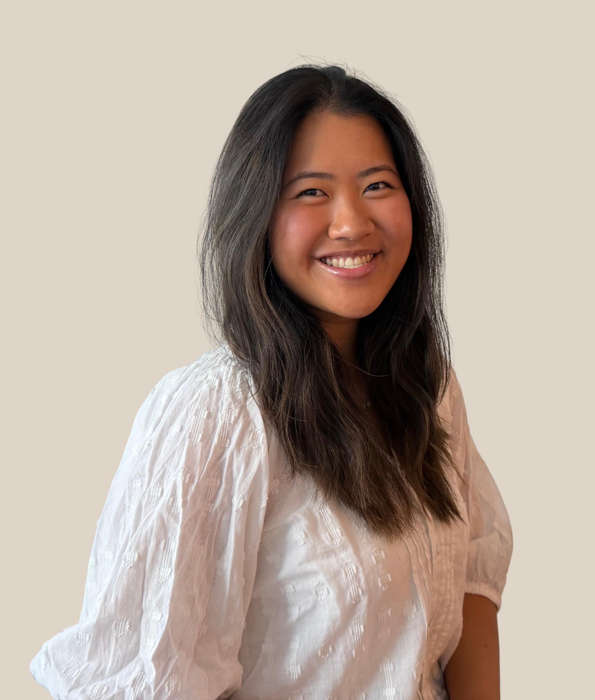Smiling woman with long dark hair wearing a light-colored, textured blouse against a light beige background.