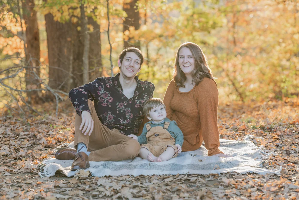 Parents and child sitting together among autumn leaves