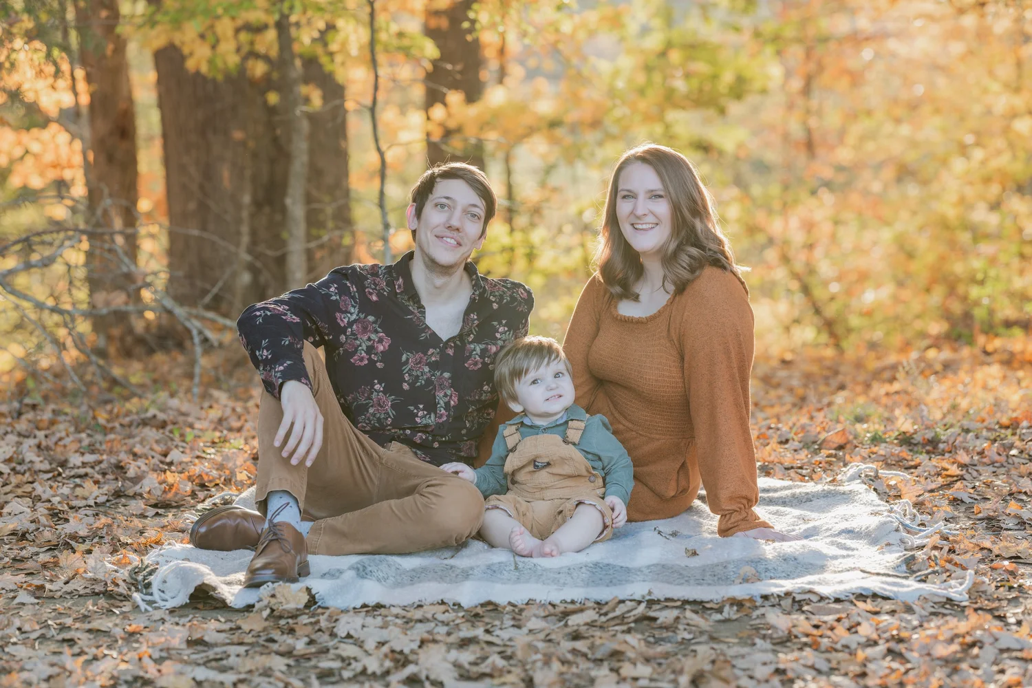 Parents and child sitting together among autumn leaves