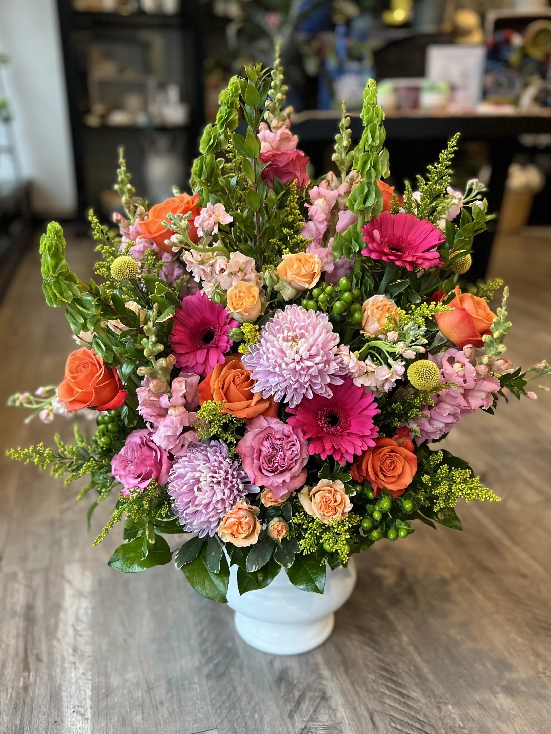Colorful flower arrangement with pink, orange, and purple flowers in a white vase on a wooden table.