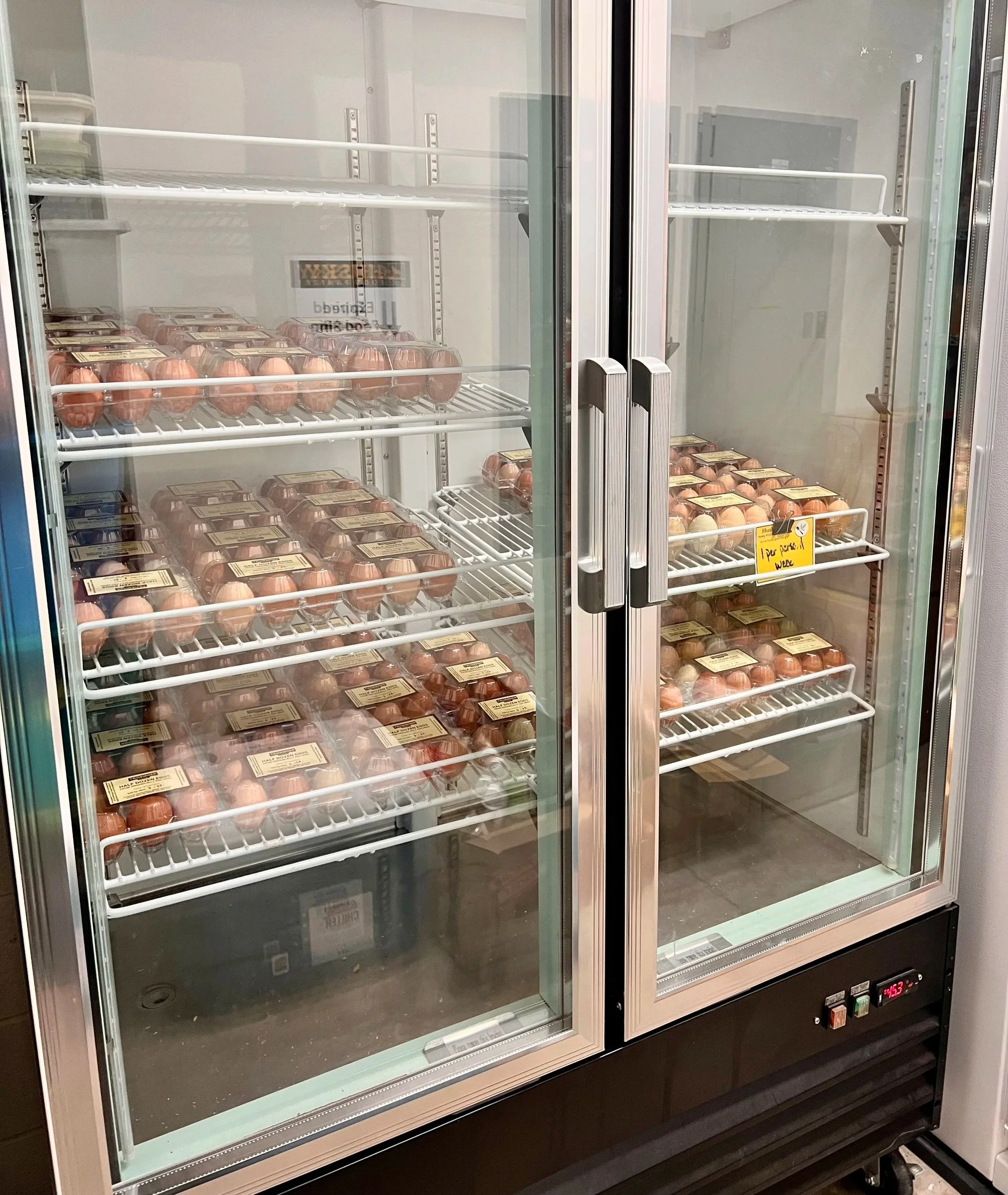 Merchandizing refrigerator with glass sliding doors, containing many cartons of eggs on the shelves.